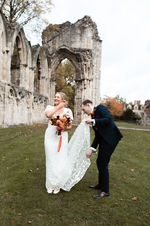A joyful wedding moment captured at ancient stone ruins with autumn foliage and gothic arches in the background.