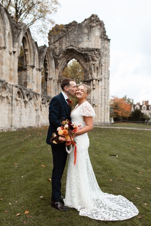 A couple shares romantic moments at historic stone abbey ruins during an autumn wedding celebration.