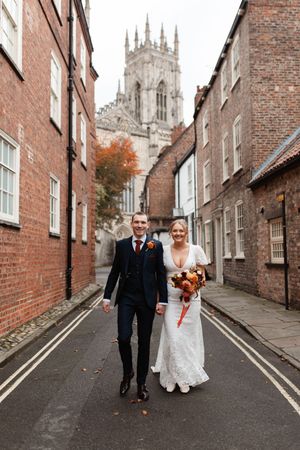 Couple walks down historic cobblestone street with York Minster cathedral rising majestically in background.