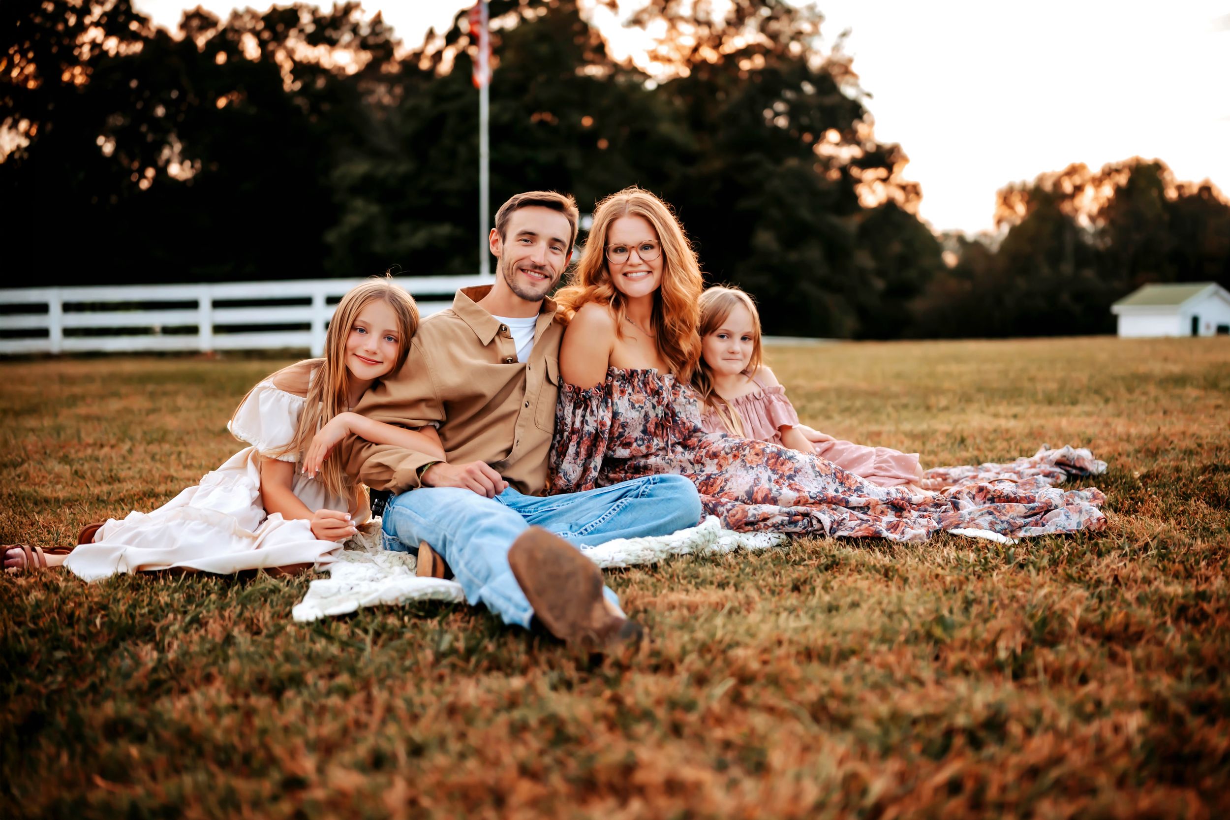 Group relaxing on blankets in a grassy field at sunset during an outdoor autumn photoshoot.