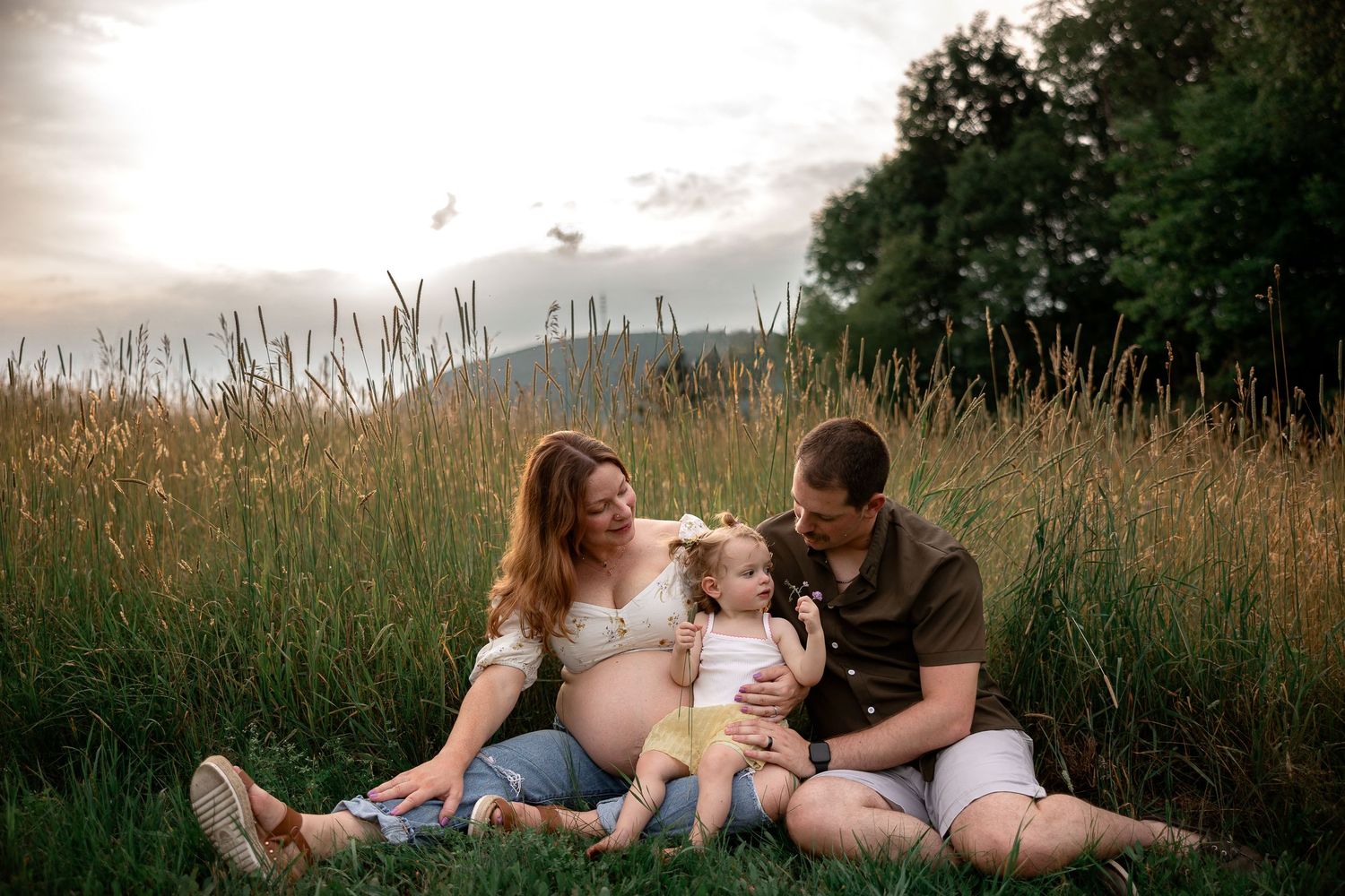 A family sits together in a golden field at sunset with tall grass and trees in the background.