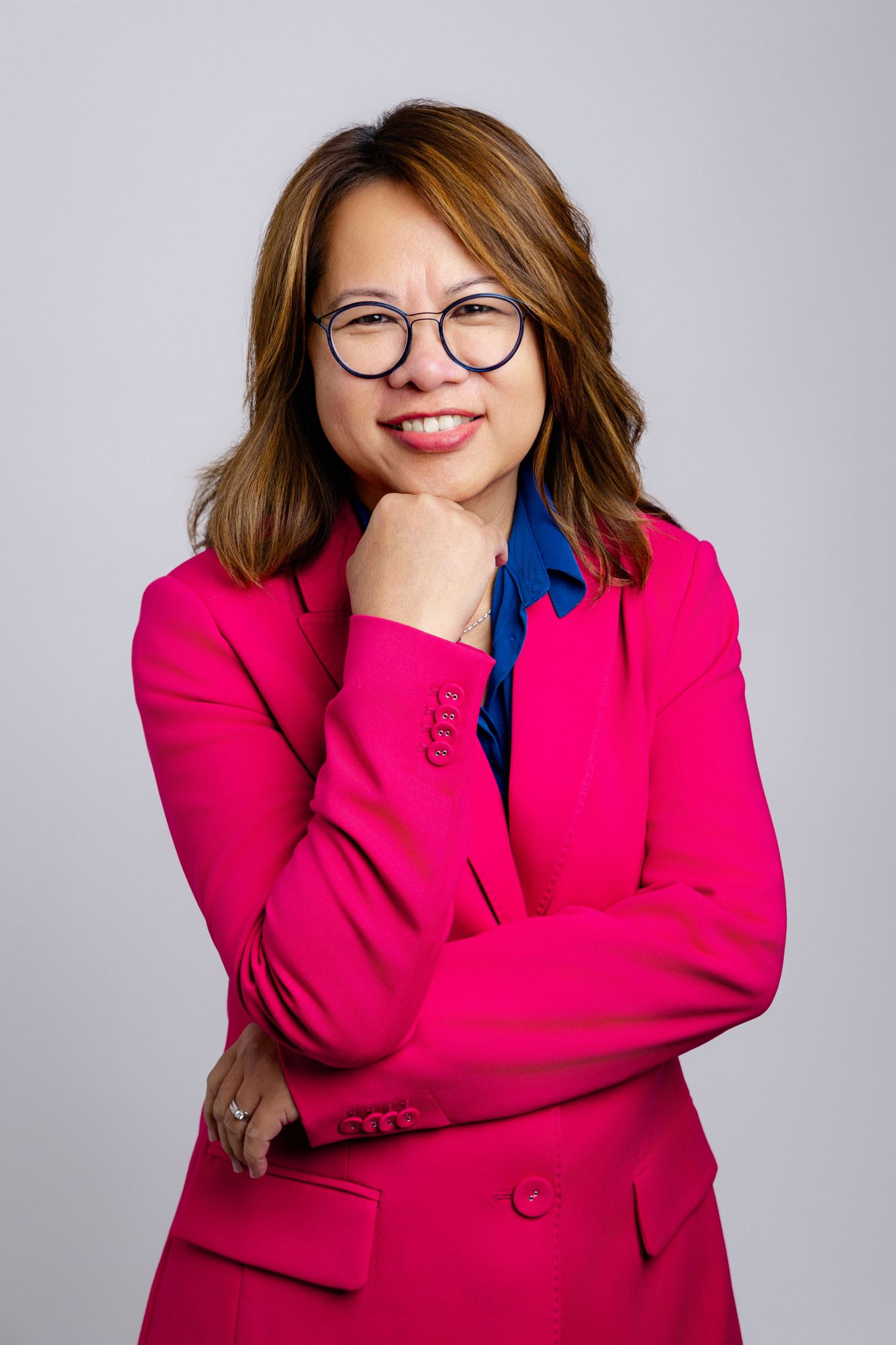 Professional wearing a vibrant pink blazer and glasses poses against a light gray background.
