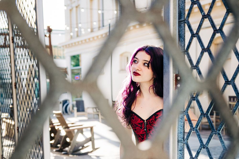 Artistic portrait with metal lattice shadows and pink haired girl highlights against a white background during Charlotte senior photos.