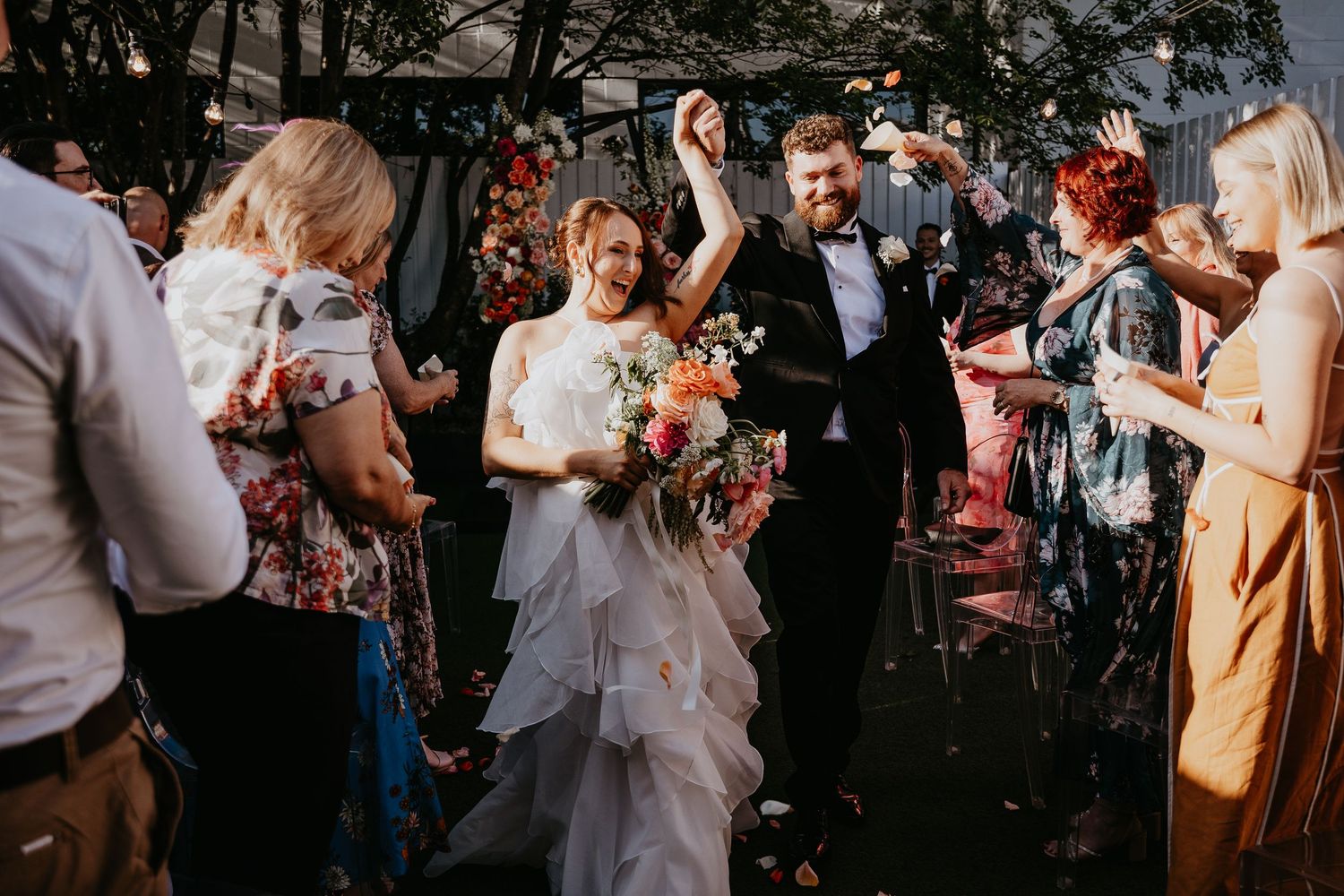 Wedding guests shower the newlyweds with confetti during an outdoor celebration as they walk down the aisle.
