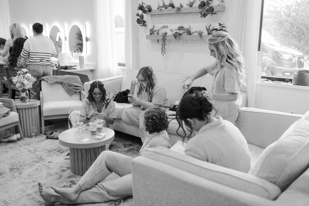 Bridal party relaxes on white couches during wedding day preparations.