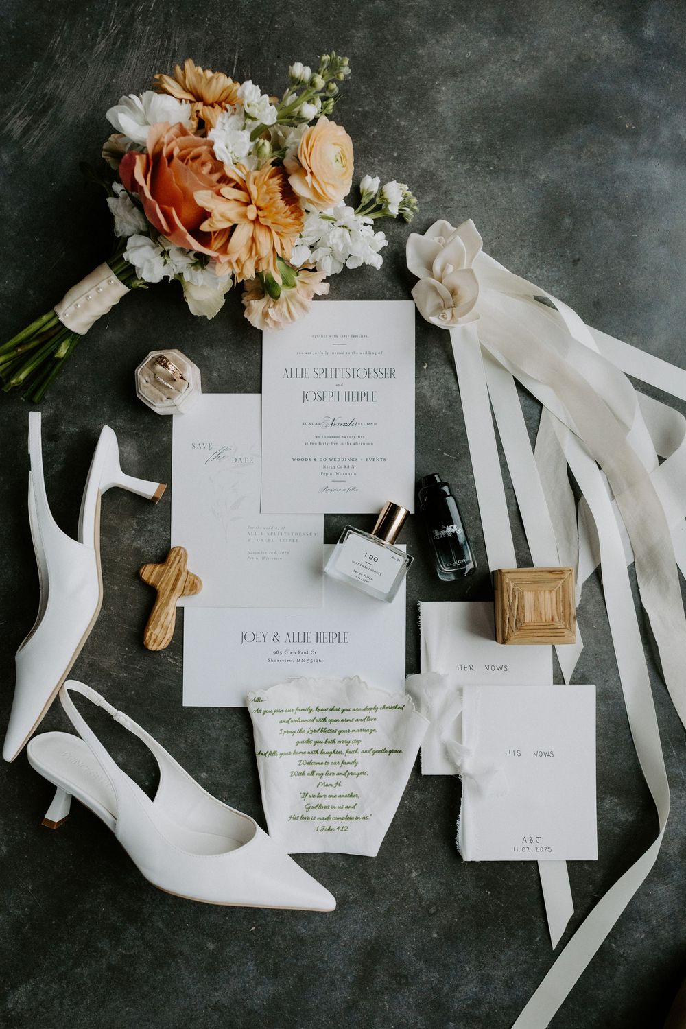 Wedding stationery flat lay with white ribbons and peach florals on dark background.