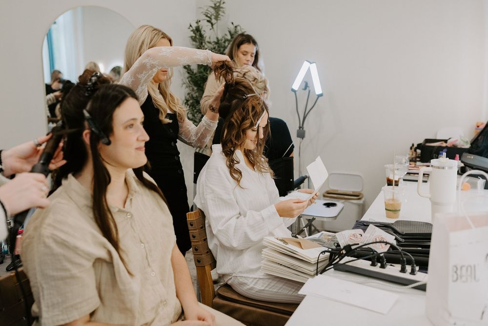 Wedding preparation scene showing makeup and hair styling in a bright white room.