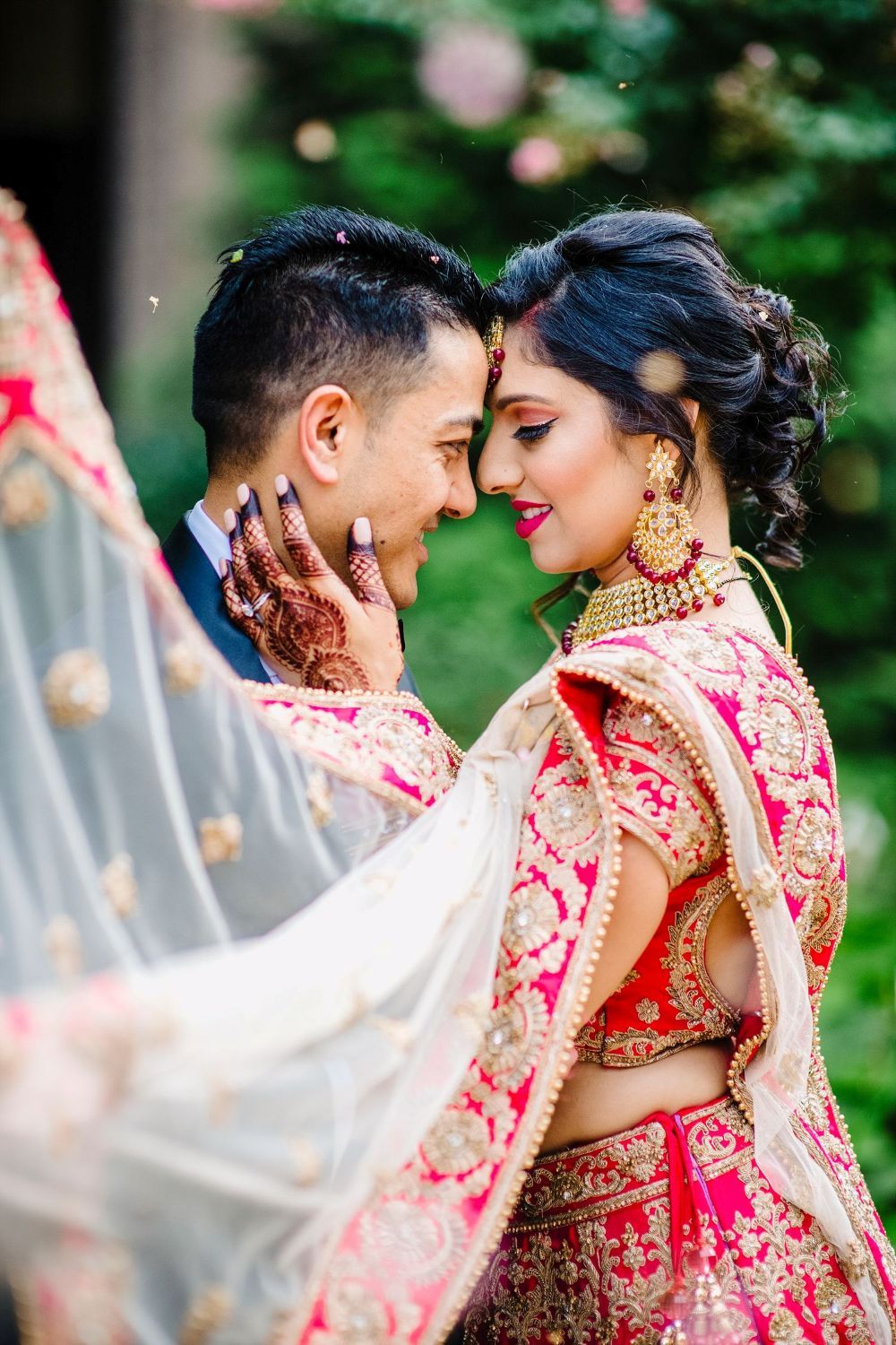 A romantic moment between newlyweds in traditional South Asian wedding attire with red and gold details.