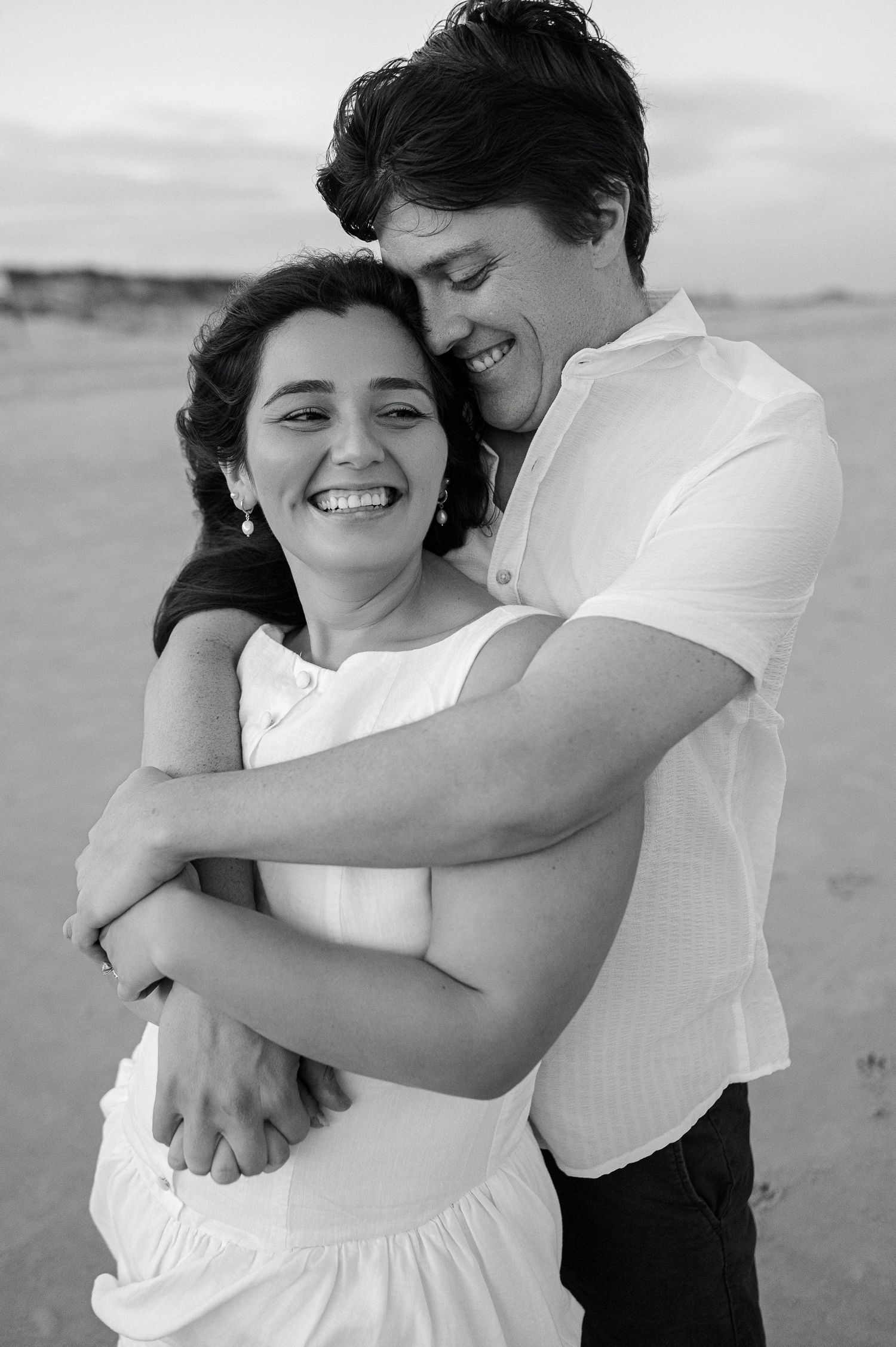 Black and white portrait of joyful couple sharing intimate embrace on beach.