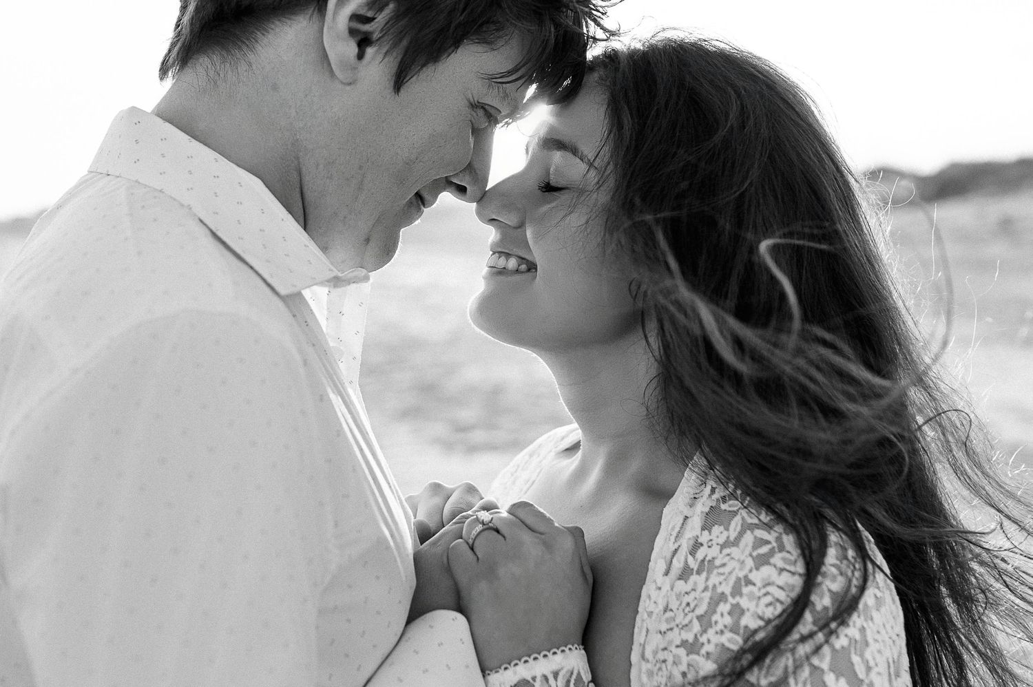 A black and white portrait captures an intimate moment between a couple on the beach.