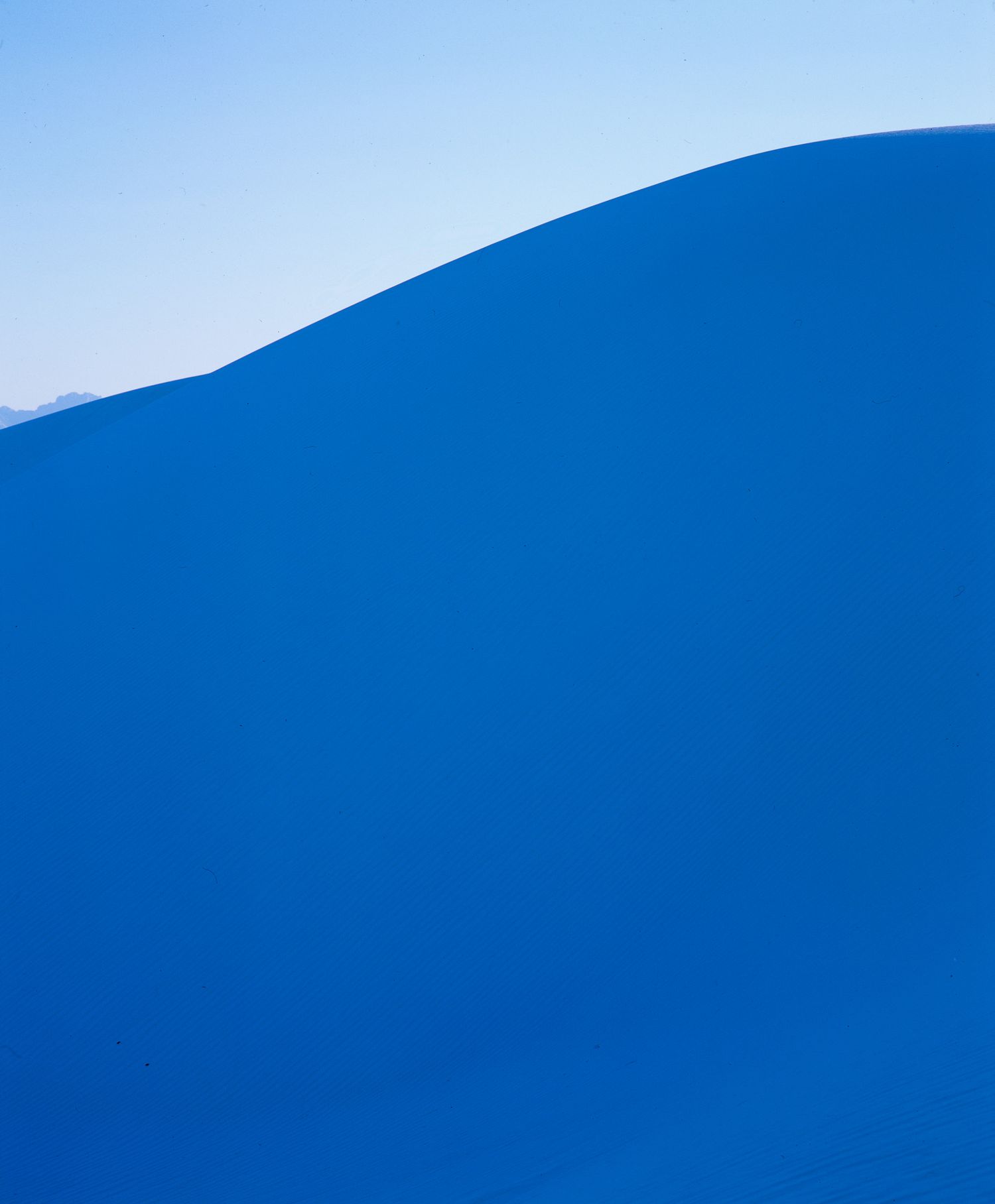 Minimalist abstract photograph of smooth blue hills against a pale blue sky.