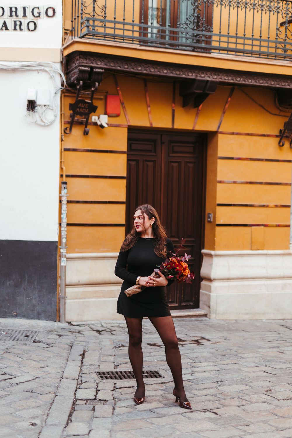 Figure in black performs dance moves on historic cobblestone street.