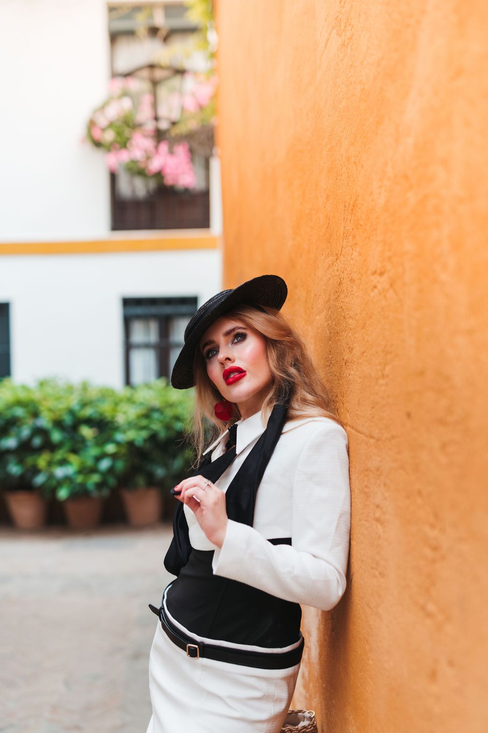 Stylish outfit with white dress, black hat, and red lipstick against an orange wall.