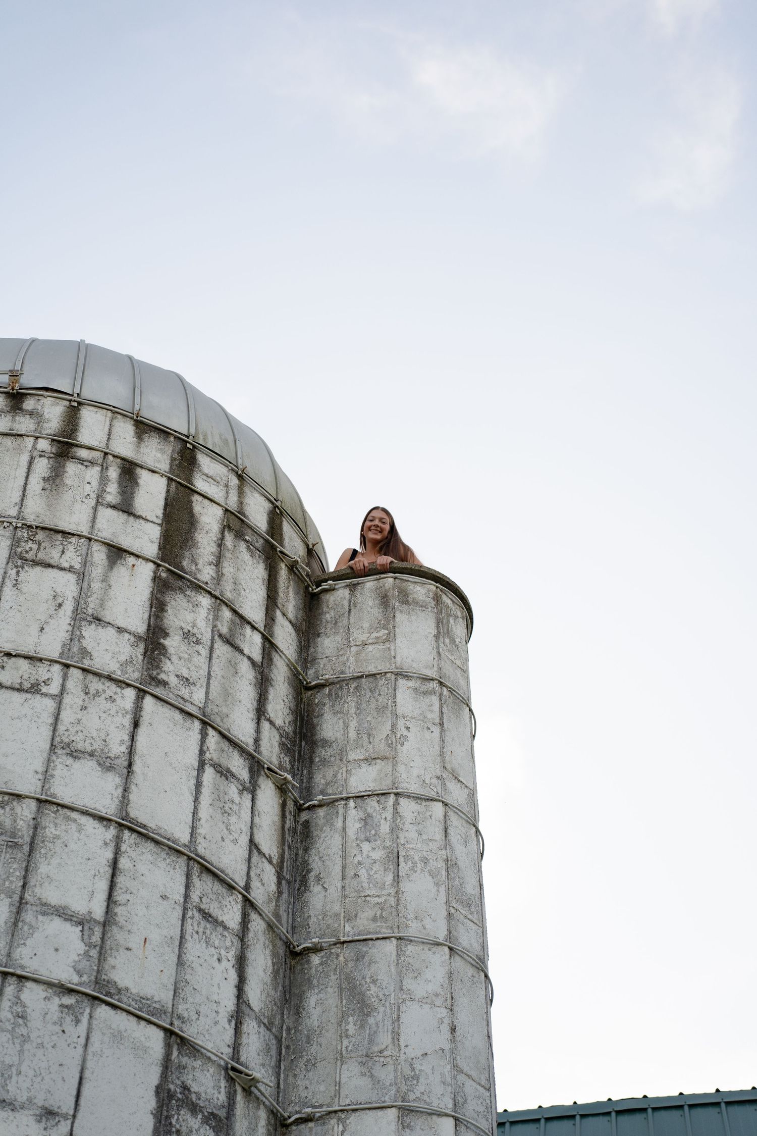 Person peeking out from top of white industrial silo against blue sky.