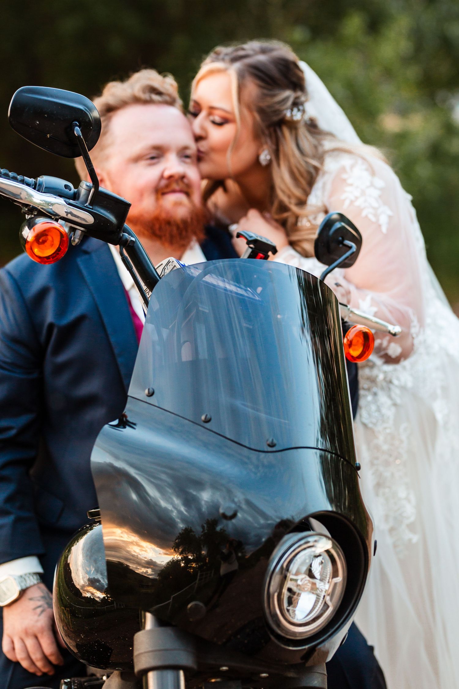 Bride kissing groom on the cheek as he sits on a motorcycle for sunset bridal portraits in Loveland, Colorado.