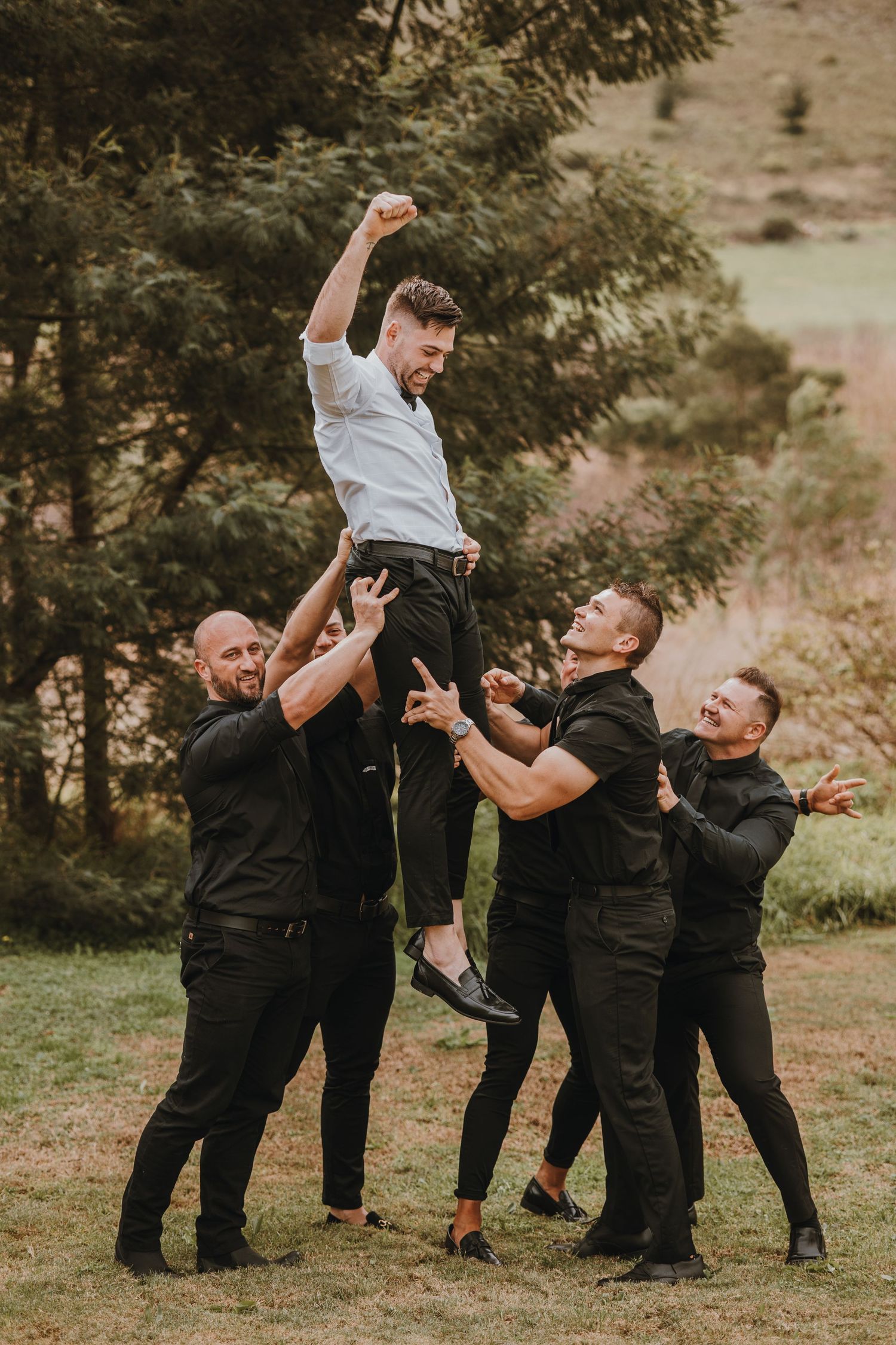 A playful sequence of groomsmen lifting and tossing the groom in celebration during an outdoor wedding photoshoot.
