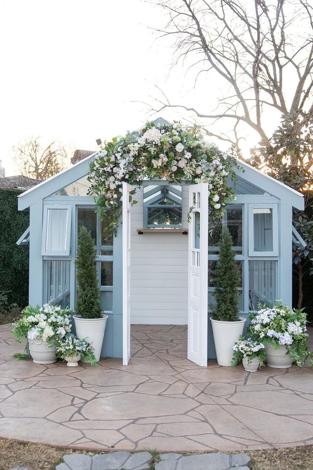 White wedding chapel facade decorated with floral arrangements and potted plants along a stone pathway at sunset.