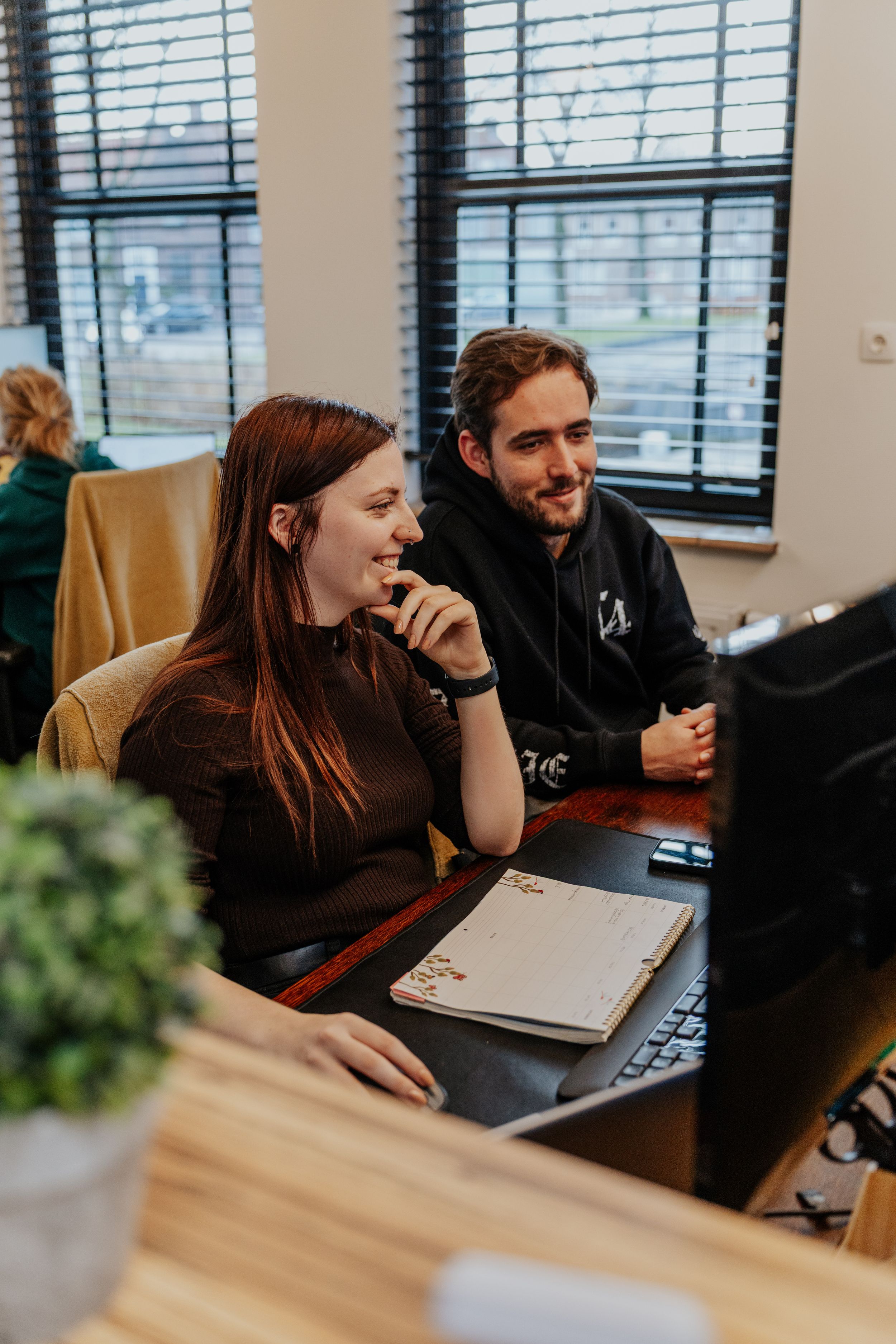 People working together and laughing in a modern office space with laptops and natural lighting.