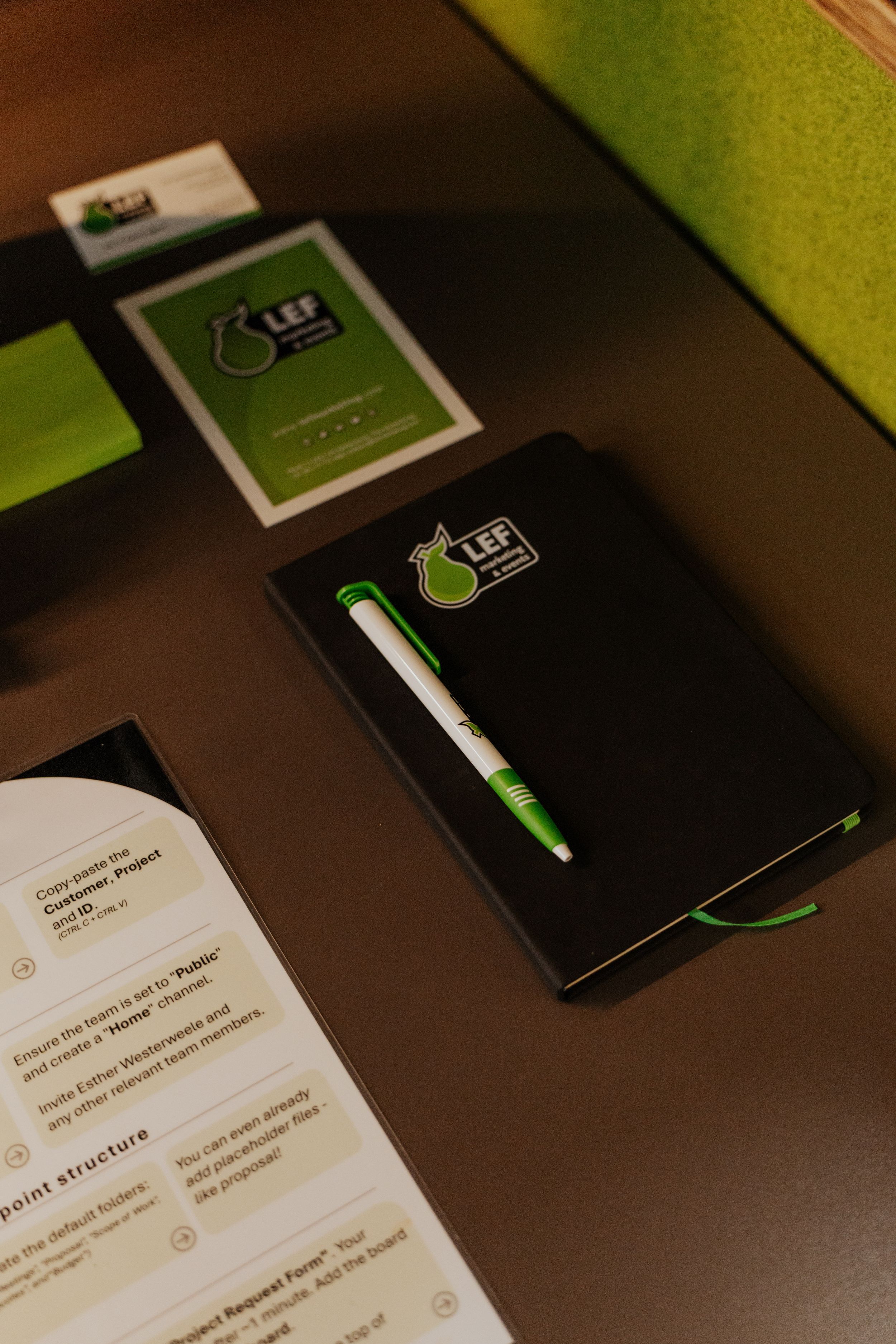 A series of black notebooks with green accents and pens arranged on a dark wooden surface in varying angles.