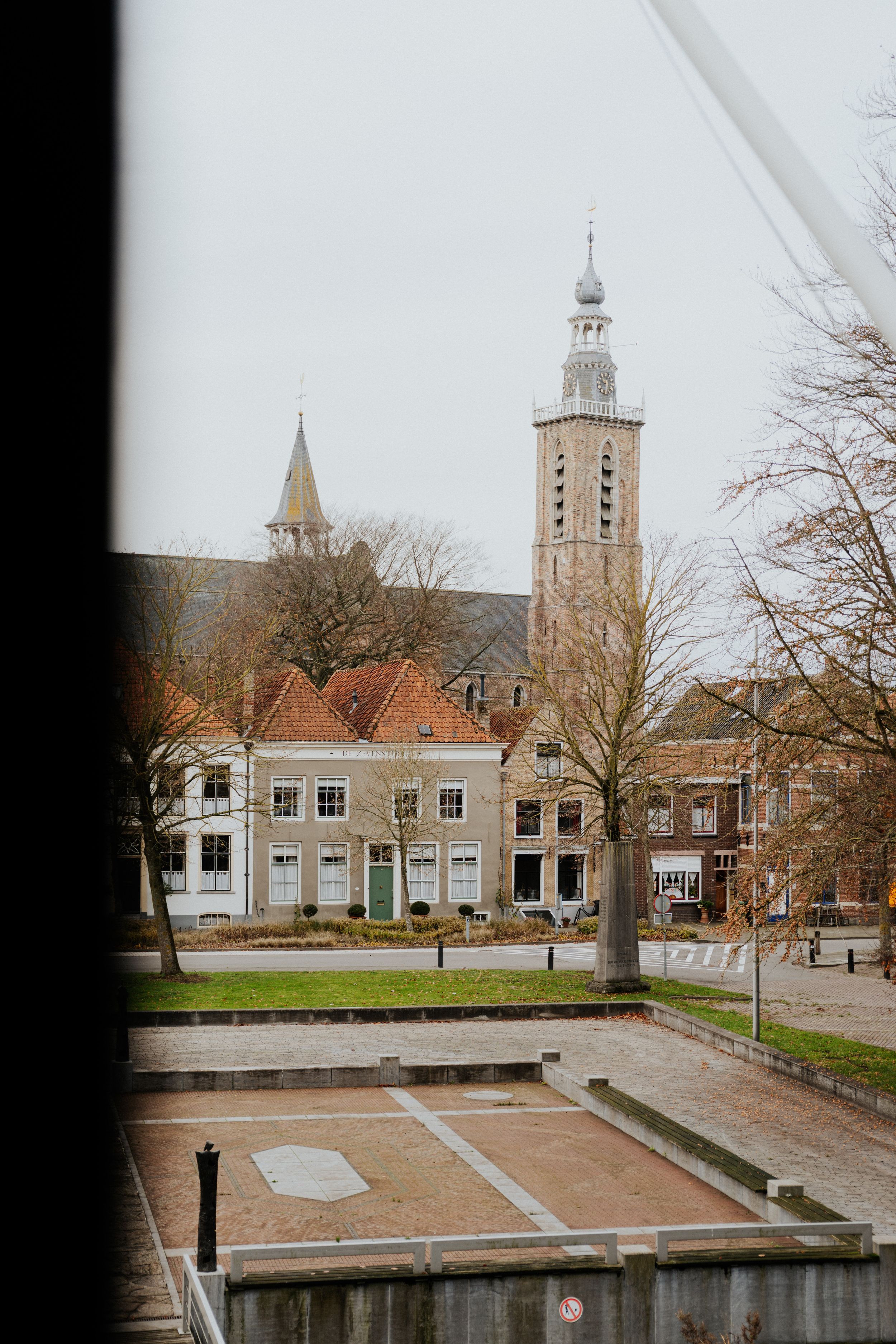 Historic Dutch town square with church tower and traditional architecture in muted tones on an overcast day.
