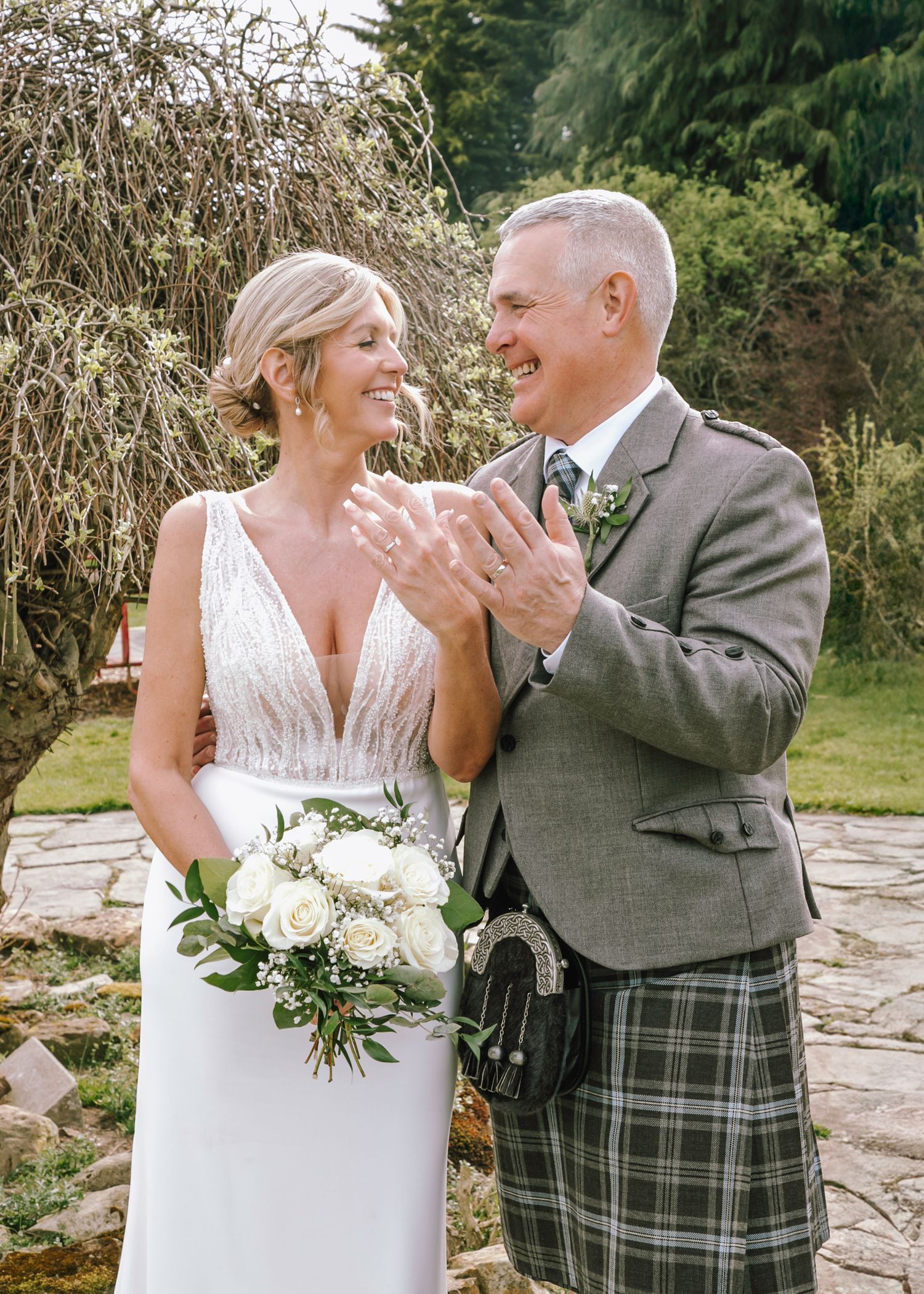 Couple laughs together during wedding portraits wearing traditional Scottish formal wear.