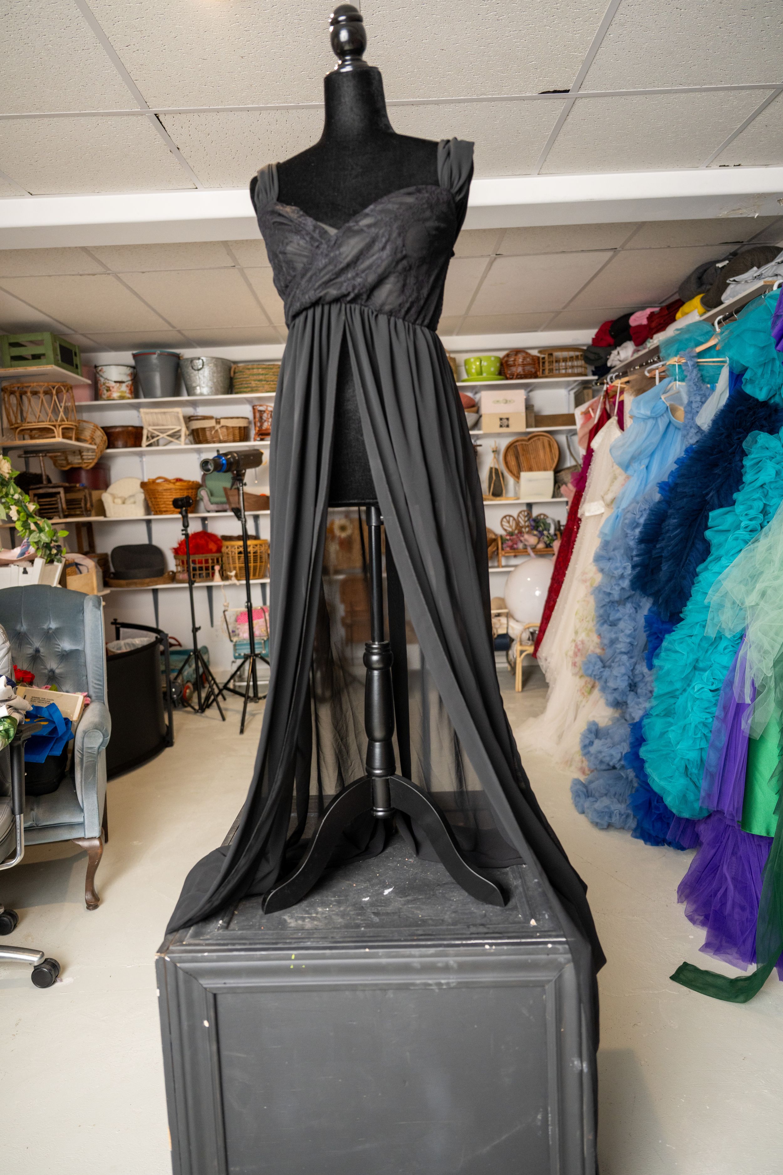 A black flowing evening gown with sweetheart neckline displayed on a mannequin in a costume storage room.