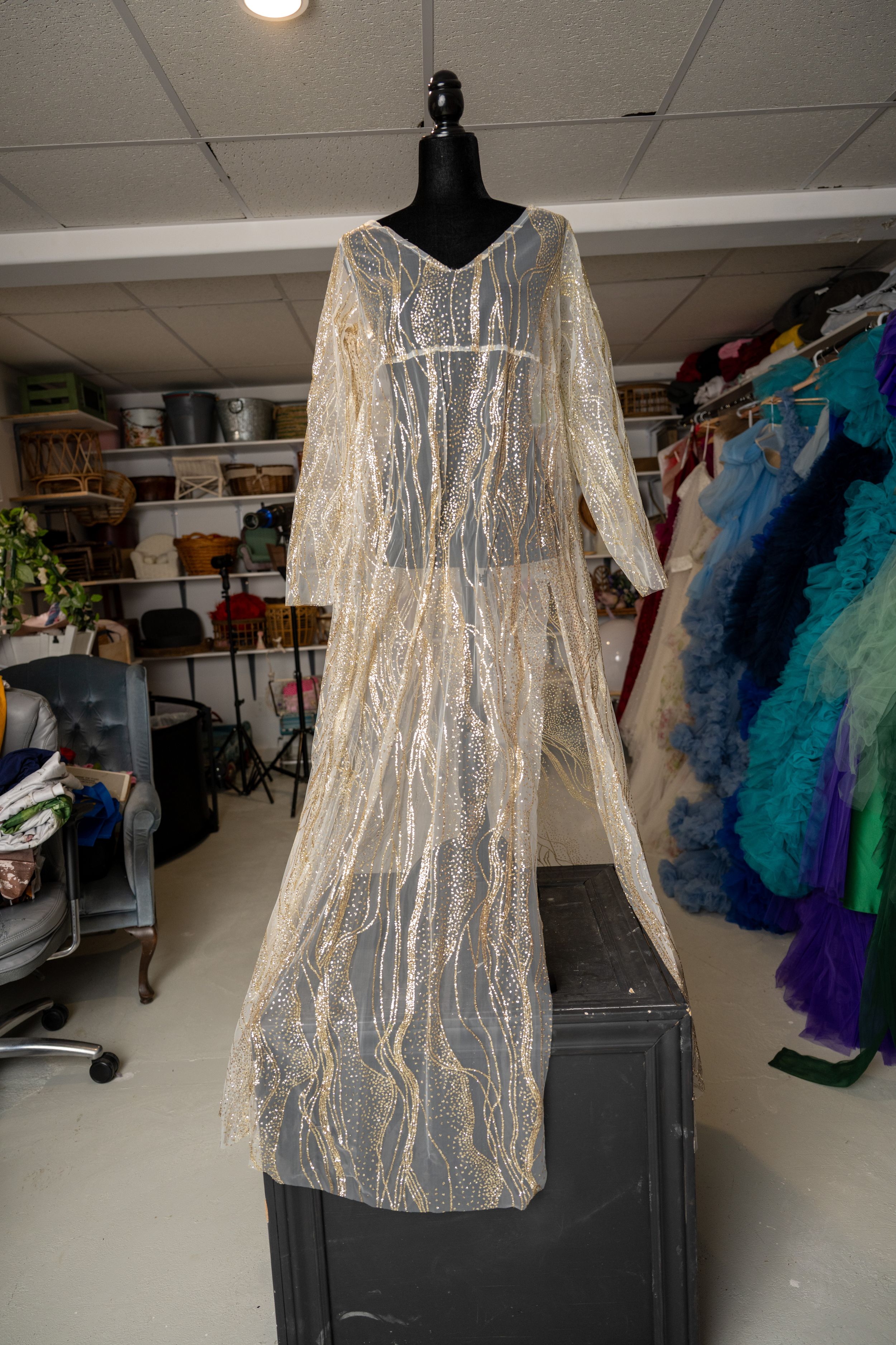 Sparkly silver sequined tunic dress displayed on black mannequin against white wall with colorful garments in background.
