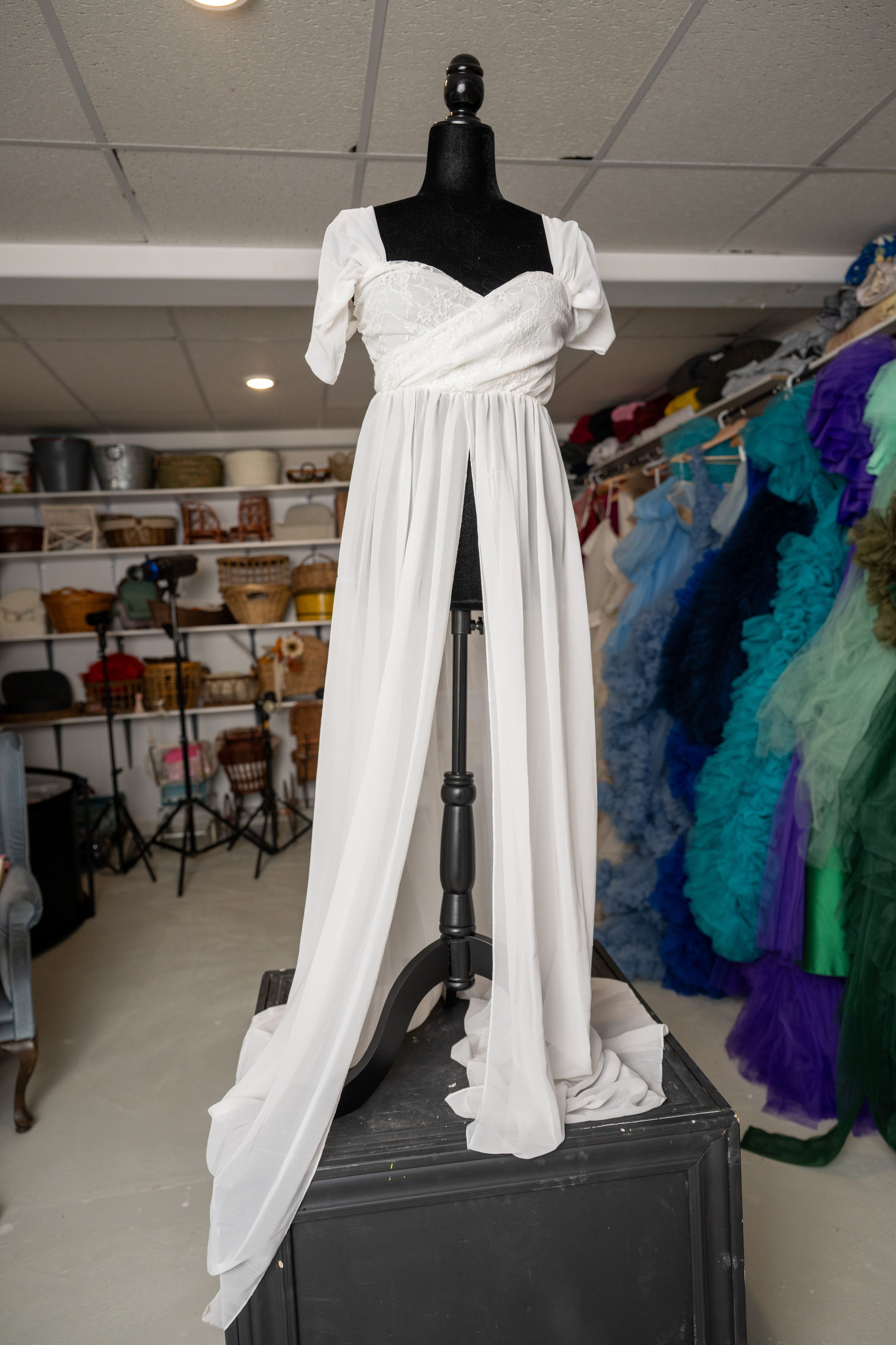 White empire waist dress with short sleeves displayed on black mannequin in costume storage room.