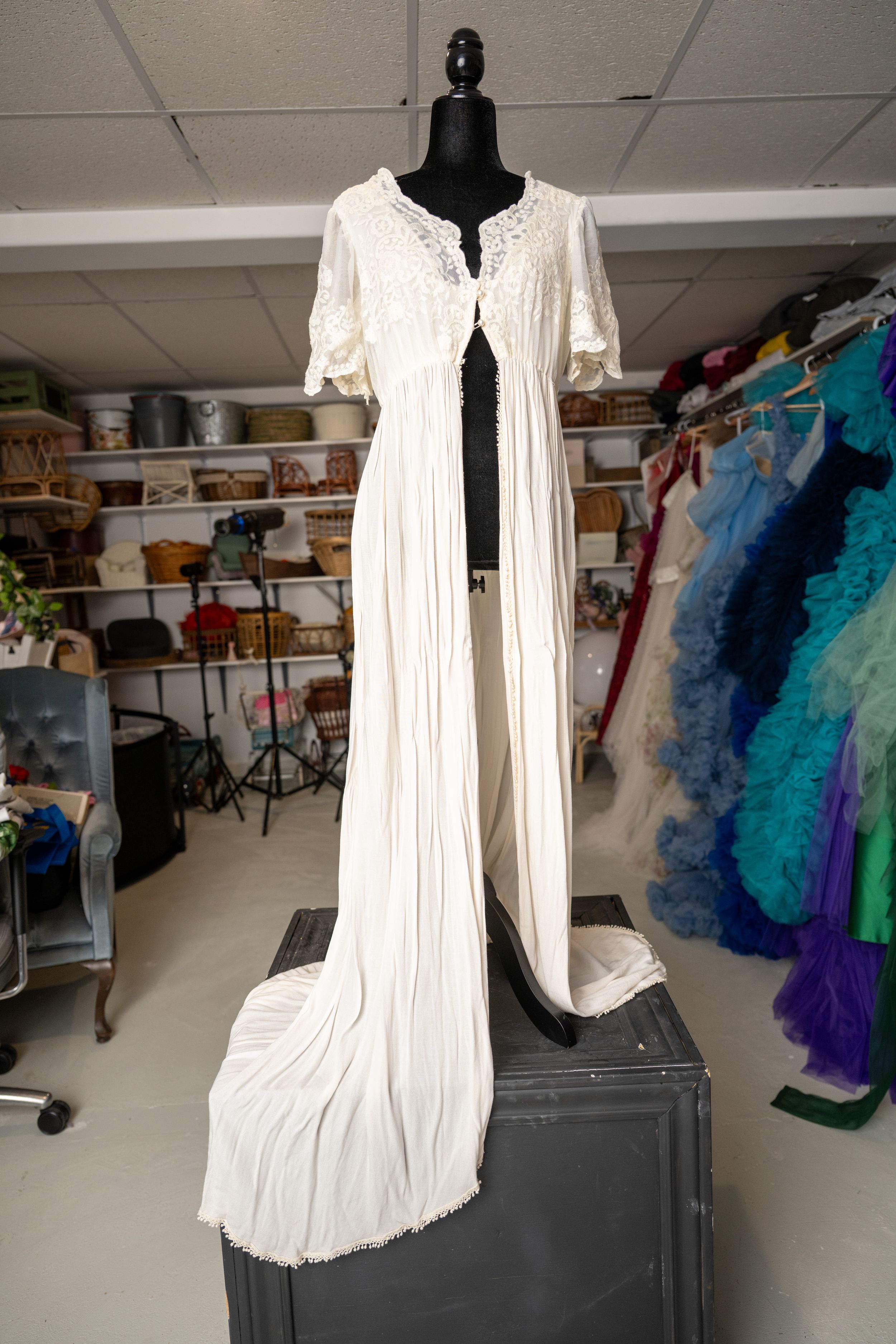White vintage-style nightgown with lace trim displayed on black mannequin in costume storage room.