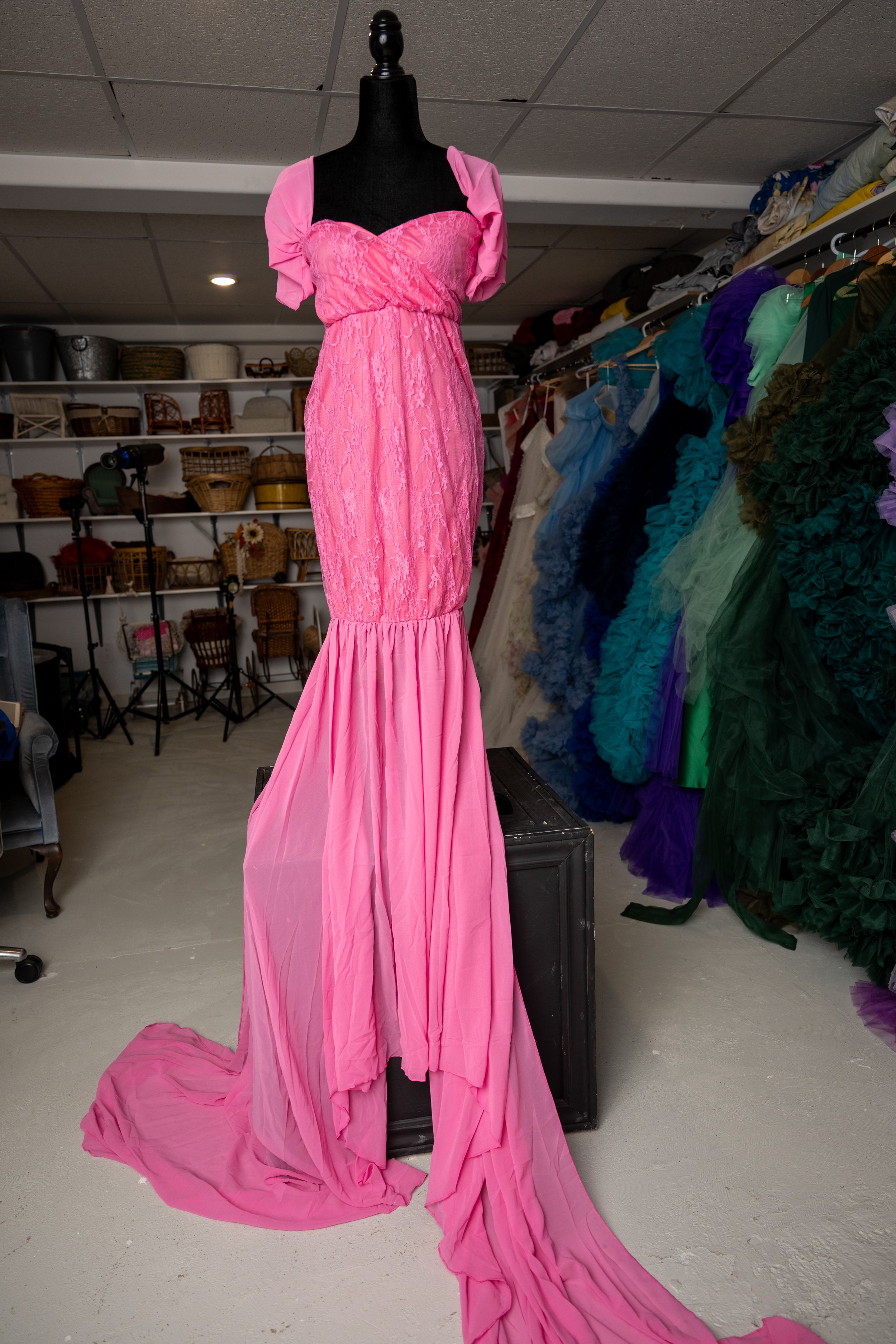 A bright pink flowing dress displayed on a black mannequin in a clothing store with other colorful dresses visible in background.