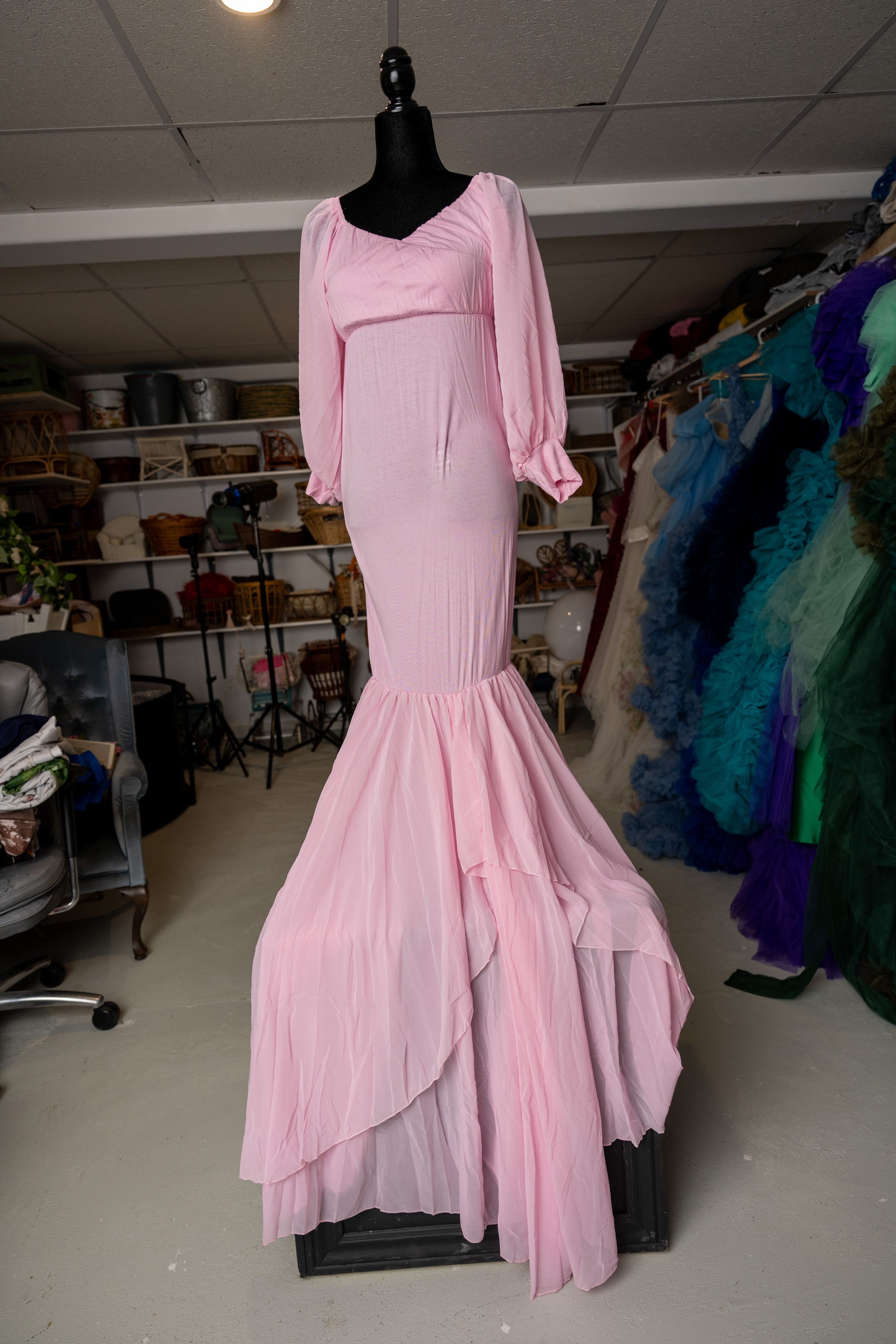 Pink mermaid-style formal gown with long puffy sleeves and layered ruffled hem displayed on mannequin in dress shop.