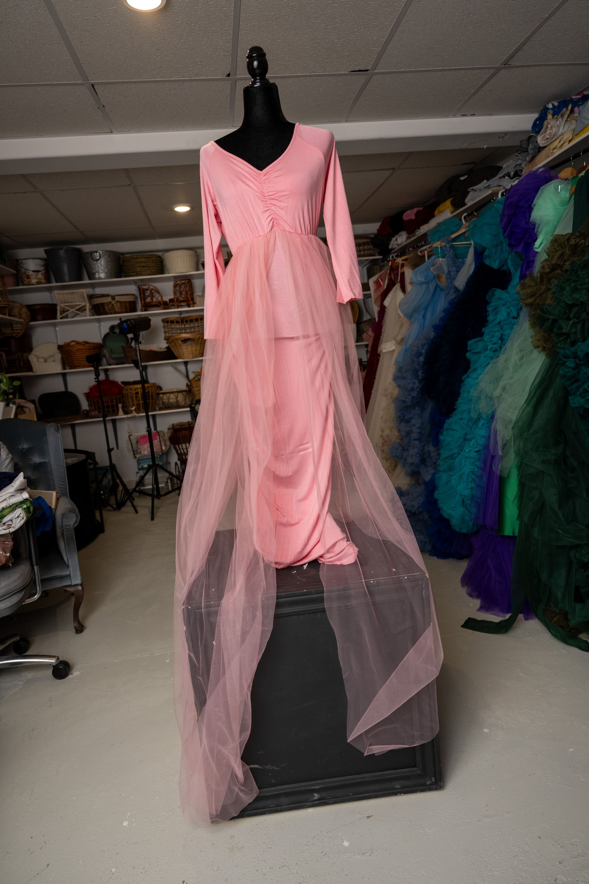 Pink dance costume with sheer flowing fabric panels displayed on black mannequin in costume storage room.