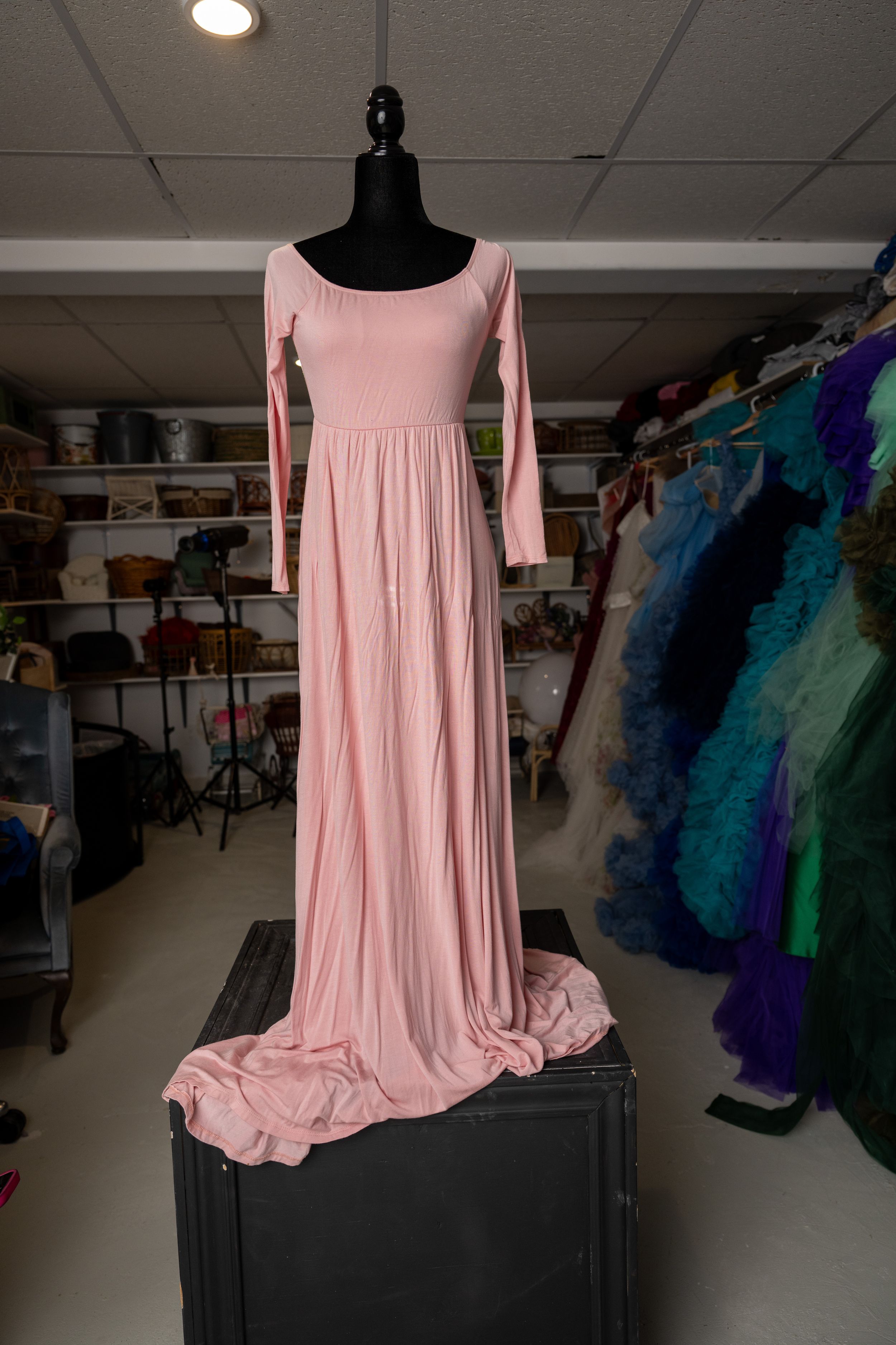 Pink flowy dance dress on black mannequin displayed in dance studio with costume racks visible in background.