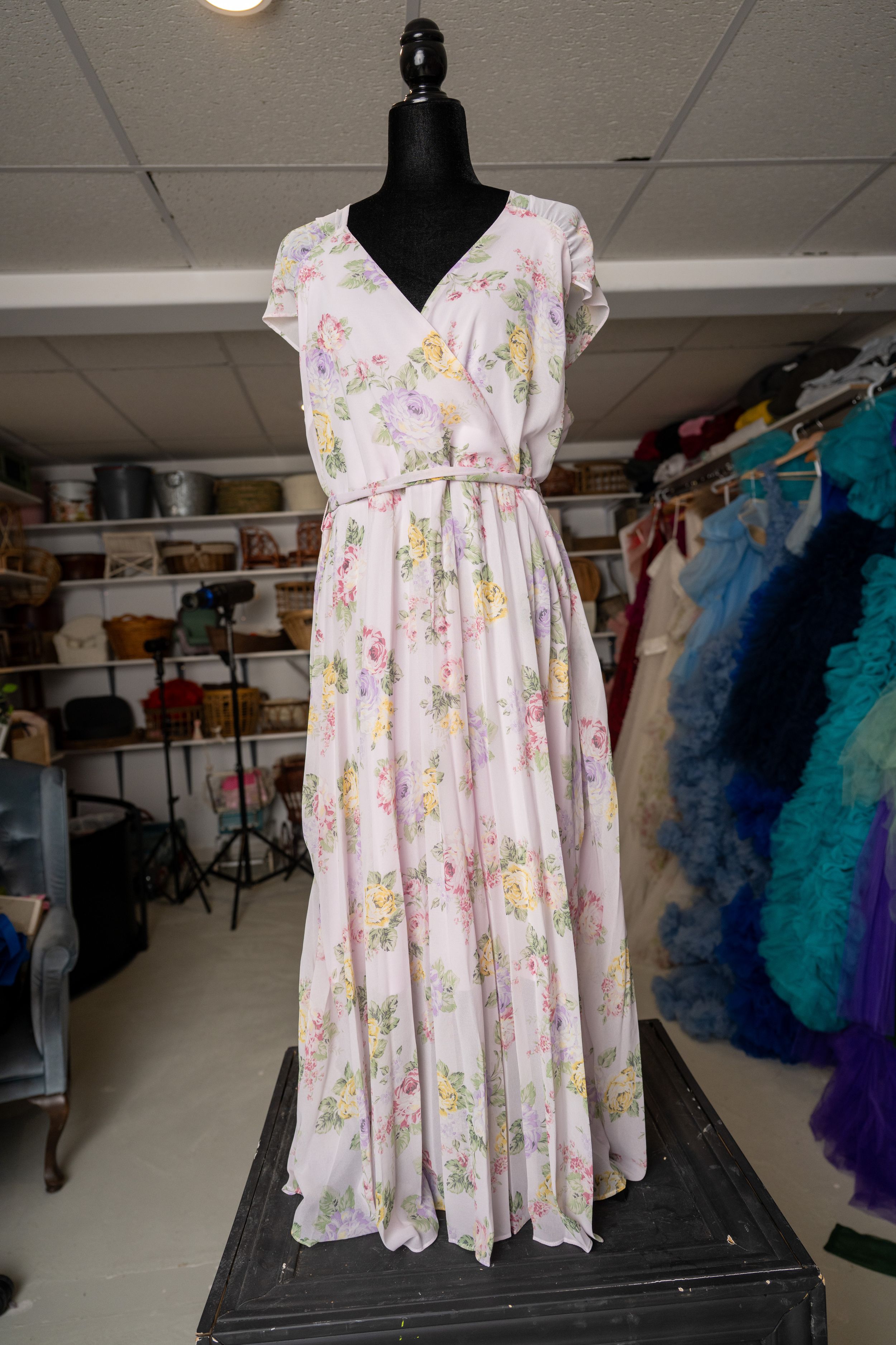 Pink floral empire waist dress with short sleeves displayed on black mannequin in clothing storage room.