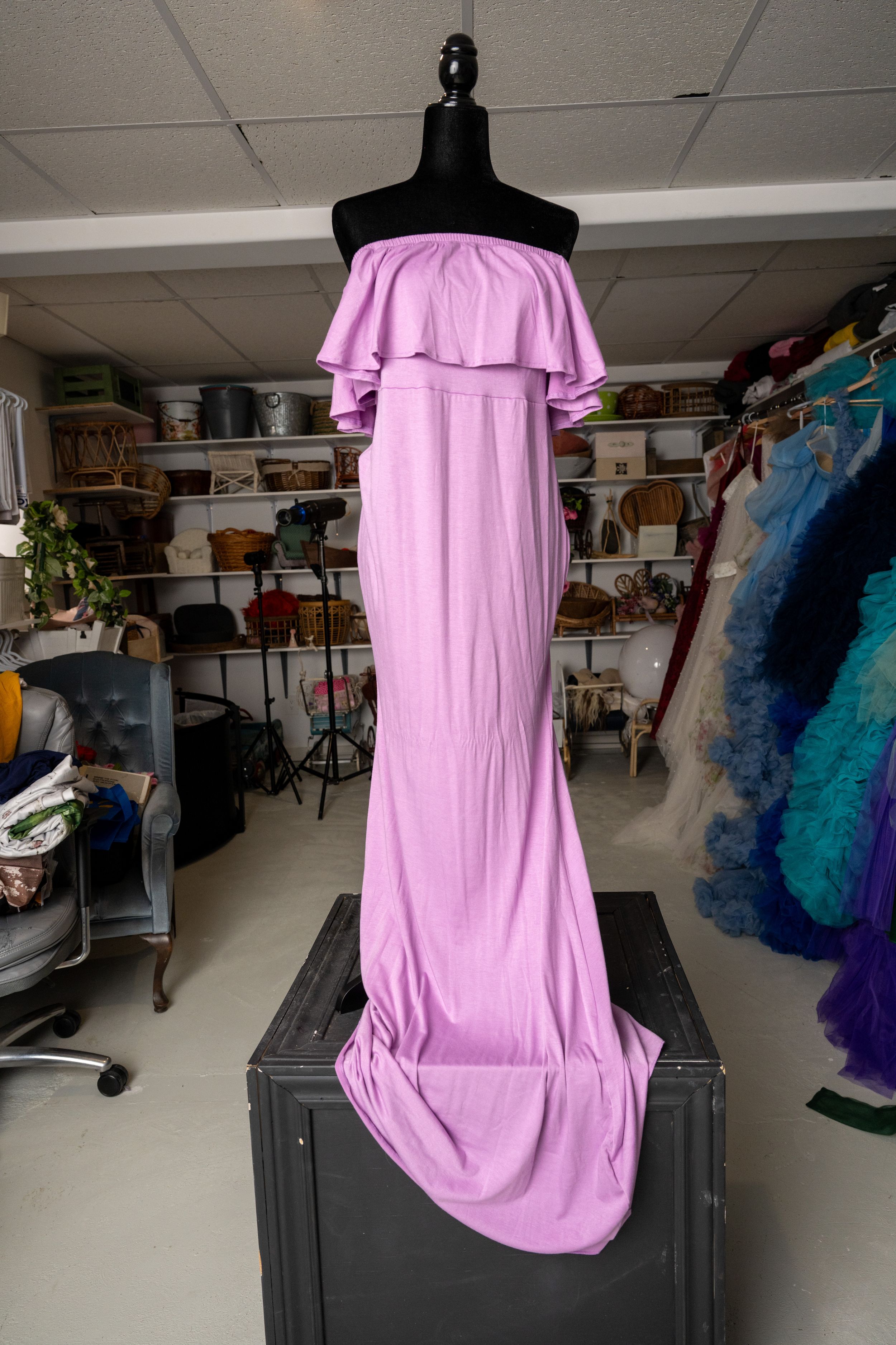 Pink off-shoulder dress displayed on a black mannequin in a studio workspace with clothing racks visible in background.