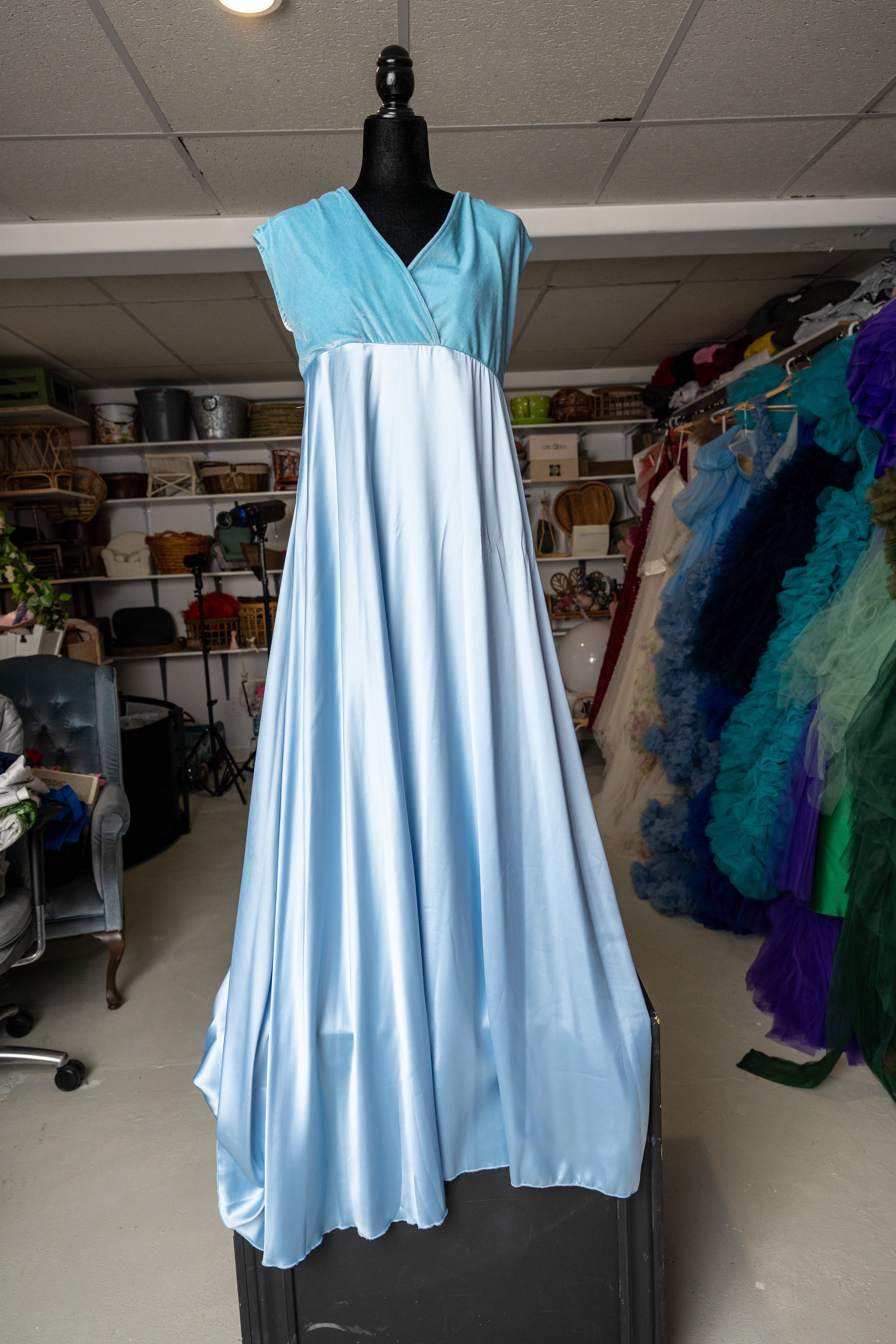 Light blue empire waist formal gown with v-neck bodice displayed on mannequin in costume storage room.