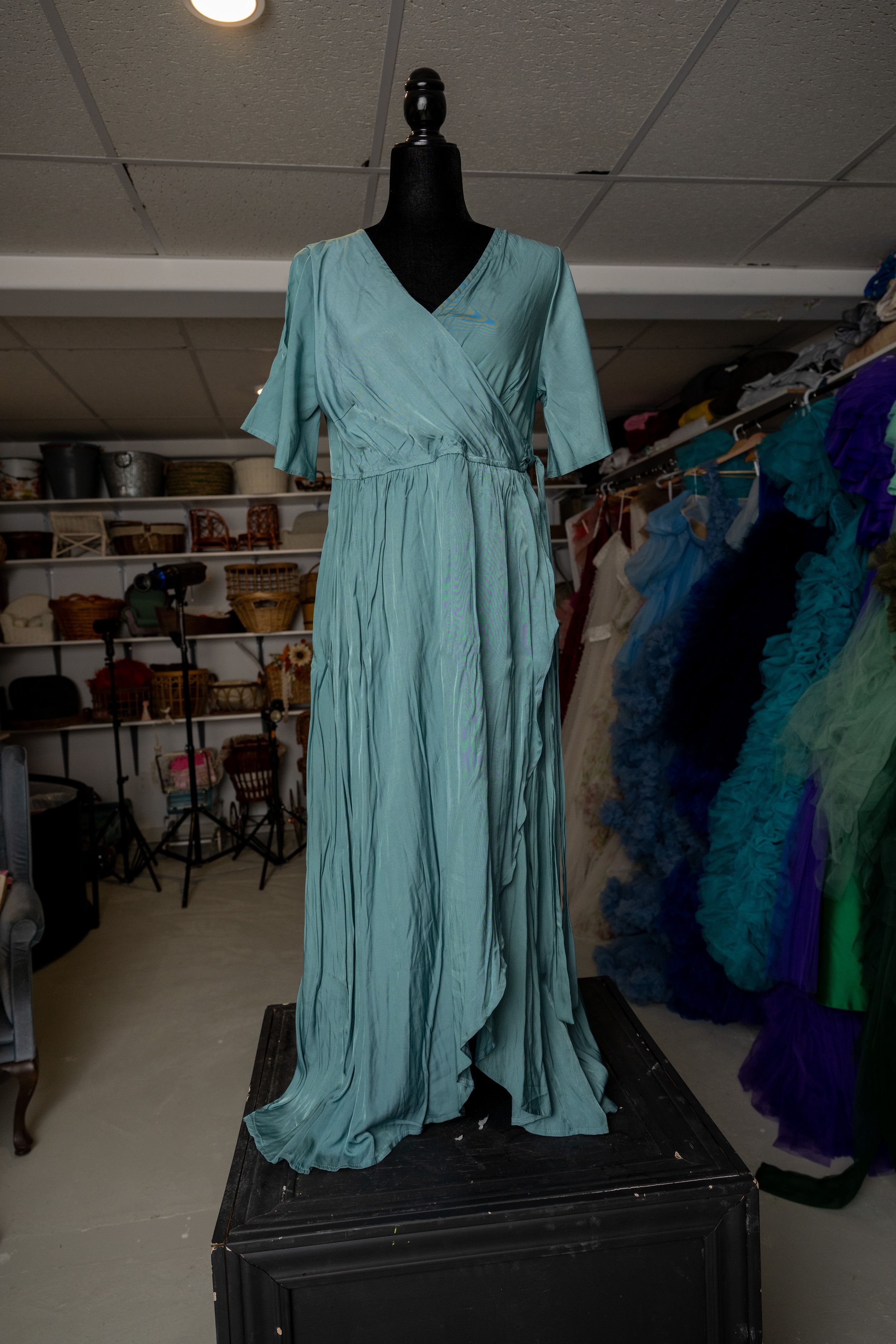 A seafoam green maxi dress with short sleeves and wrap style displayed on a black mannequin in a clothing store.