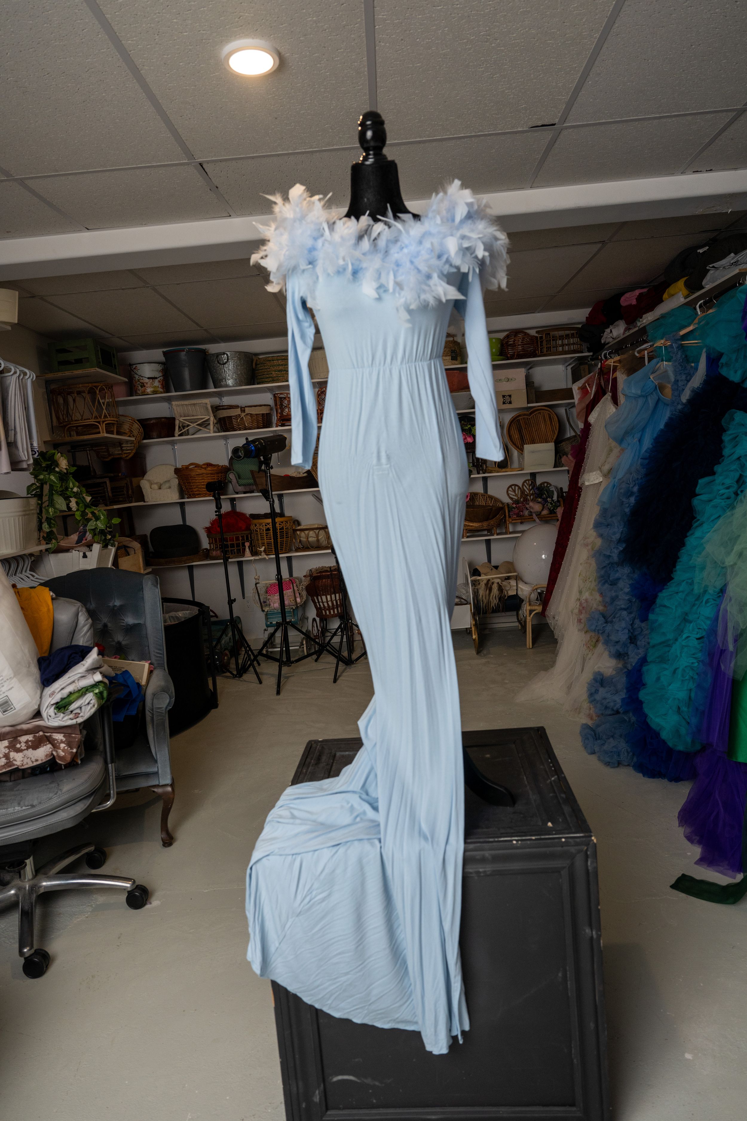 A long white evening gown with feather trim displayed on a mannequin in a costume storage room.