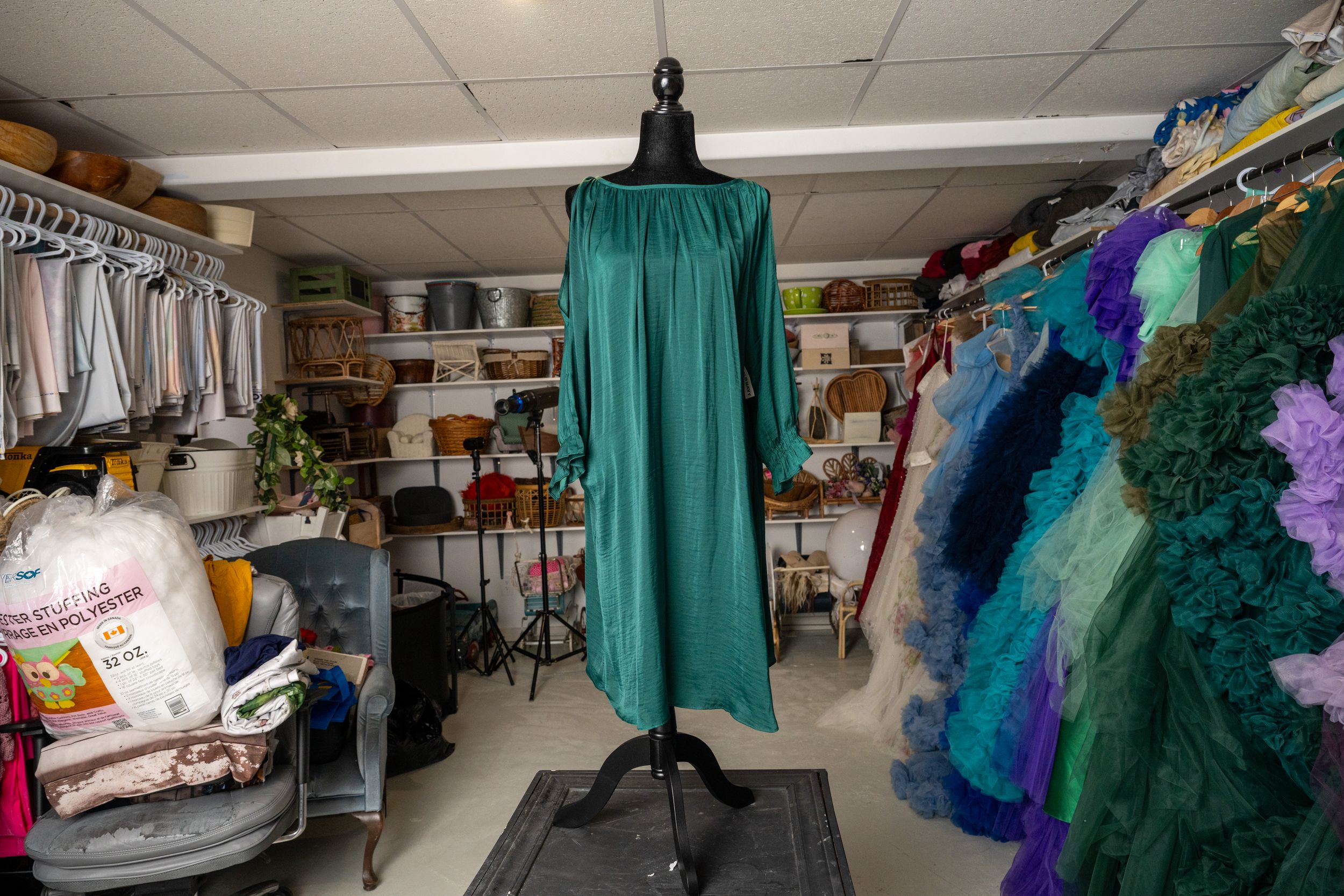 A panoramic view of a costume storage room with racks of colorful theatrical garments and turquoise curtains.