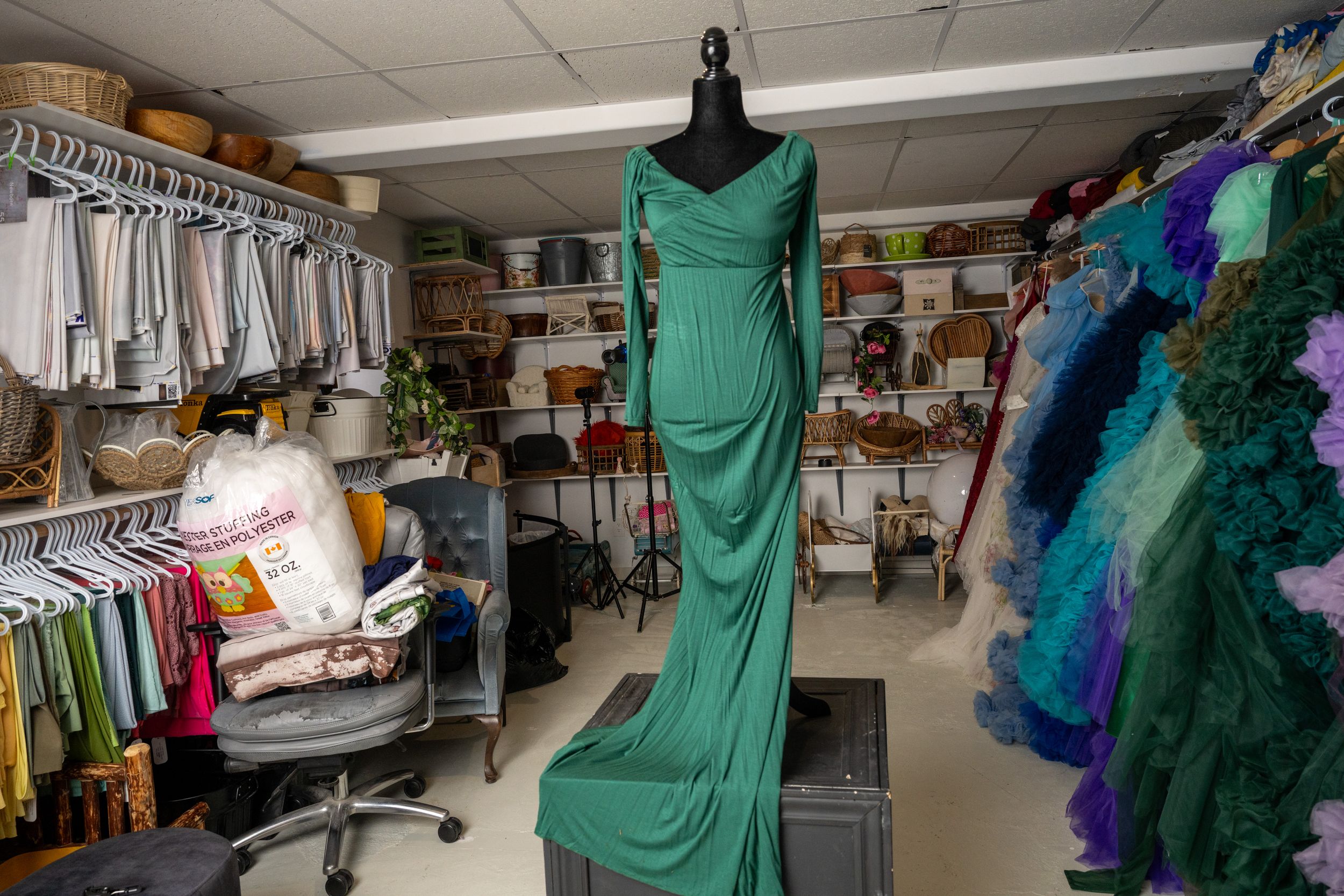 Retail store interior displaying rows of formal dresses and gowns in green, blue and other colors on clothing racks.