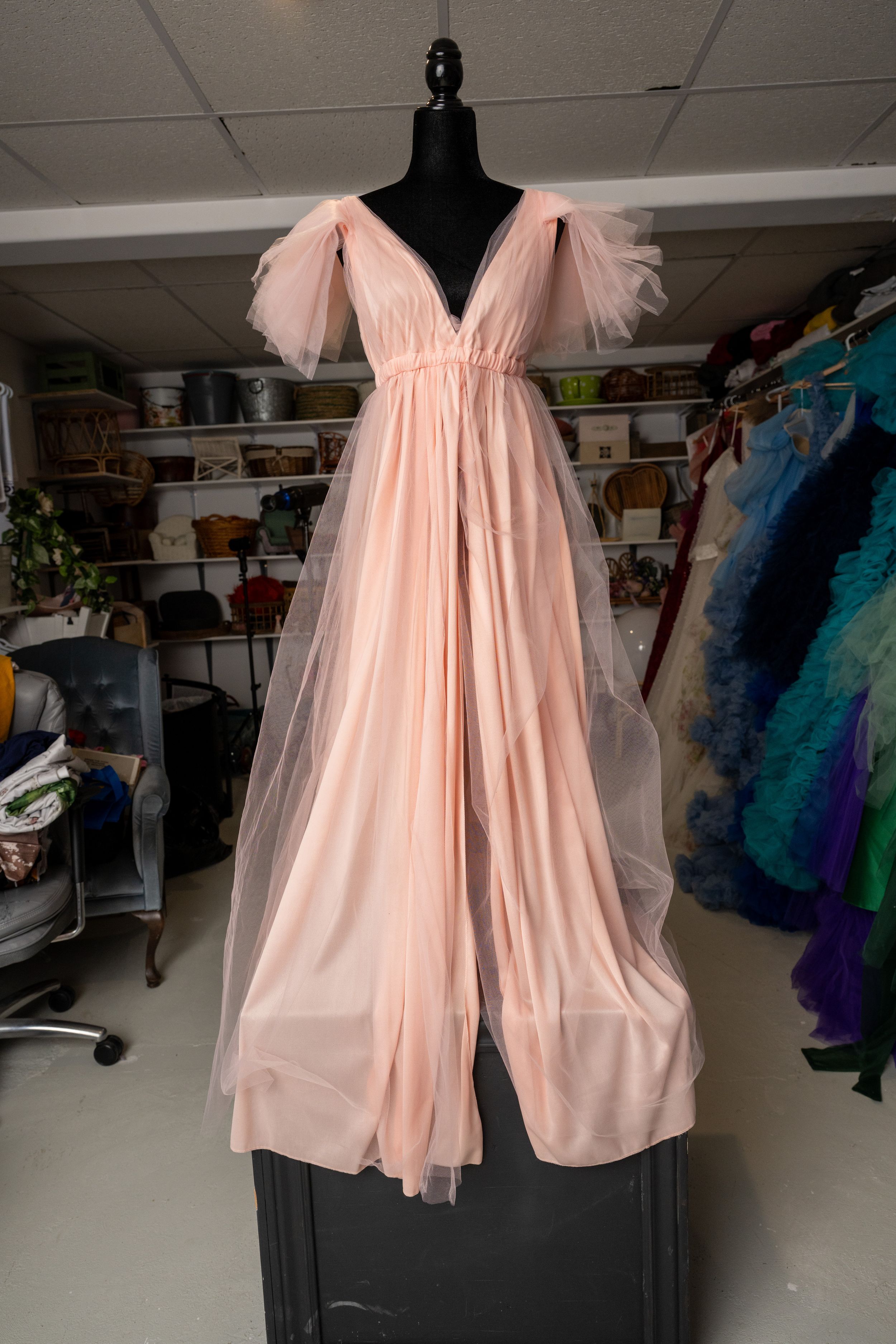 A series of pale pink tulle and chiffon dresses displayed on mannequins in a costume or fashion workspace.