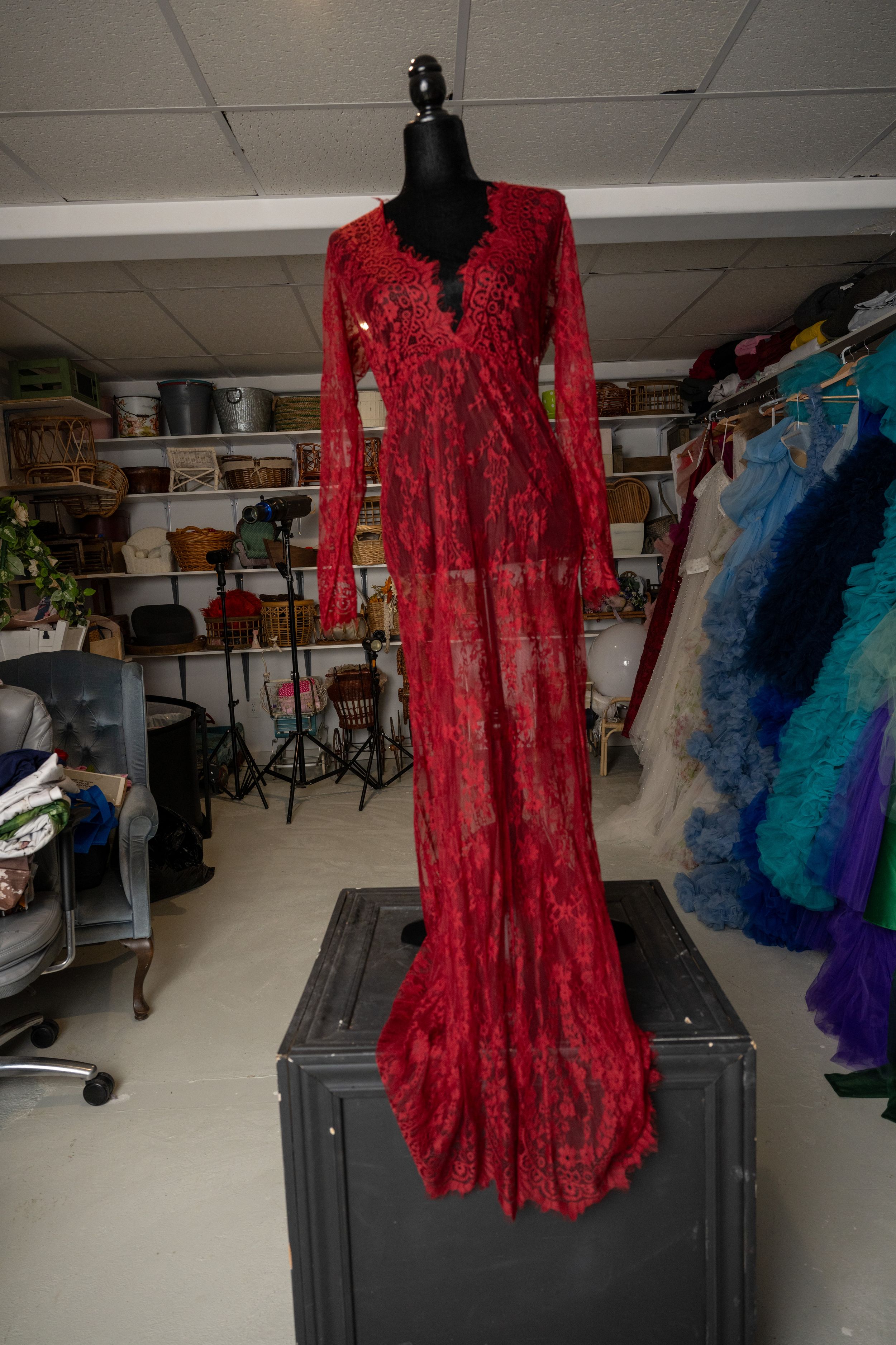 A red crushed velvet medieval-style dress displayed on a black mannequin in a costume storage room.