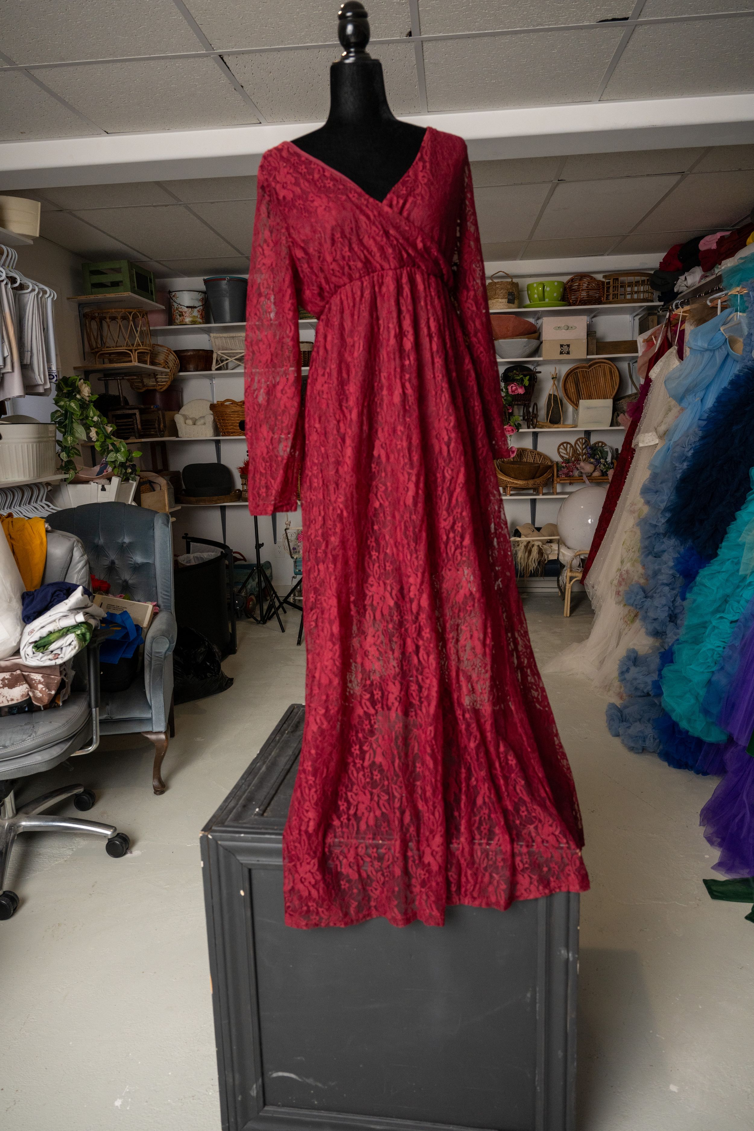 Red lace dress with long sleeves displayed on black mannequin in storage room with shelving and clothing racks.