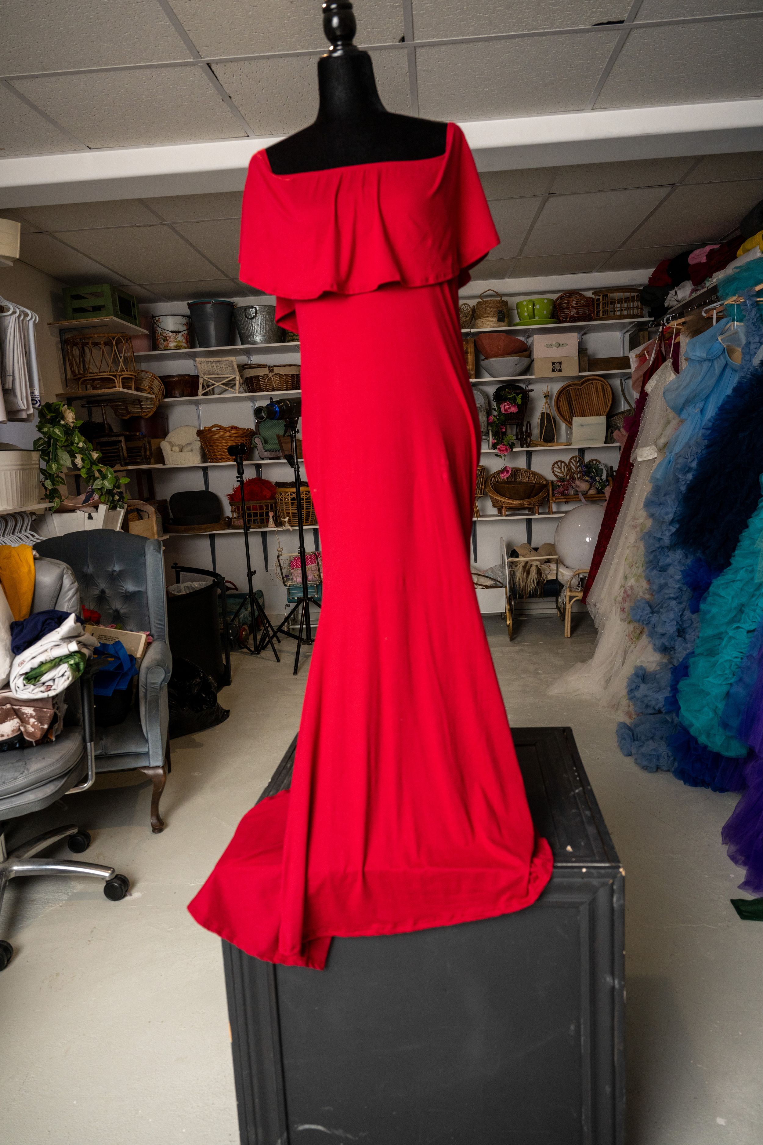 Red dress displayed on a mannequin in a cluttered storage room with shelving and supplies visible in background.