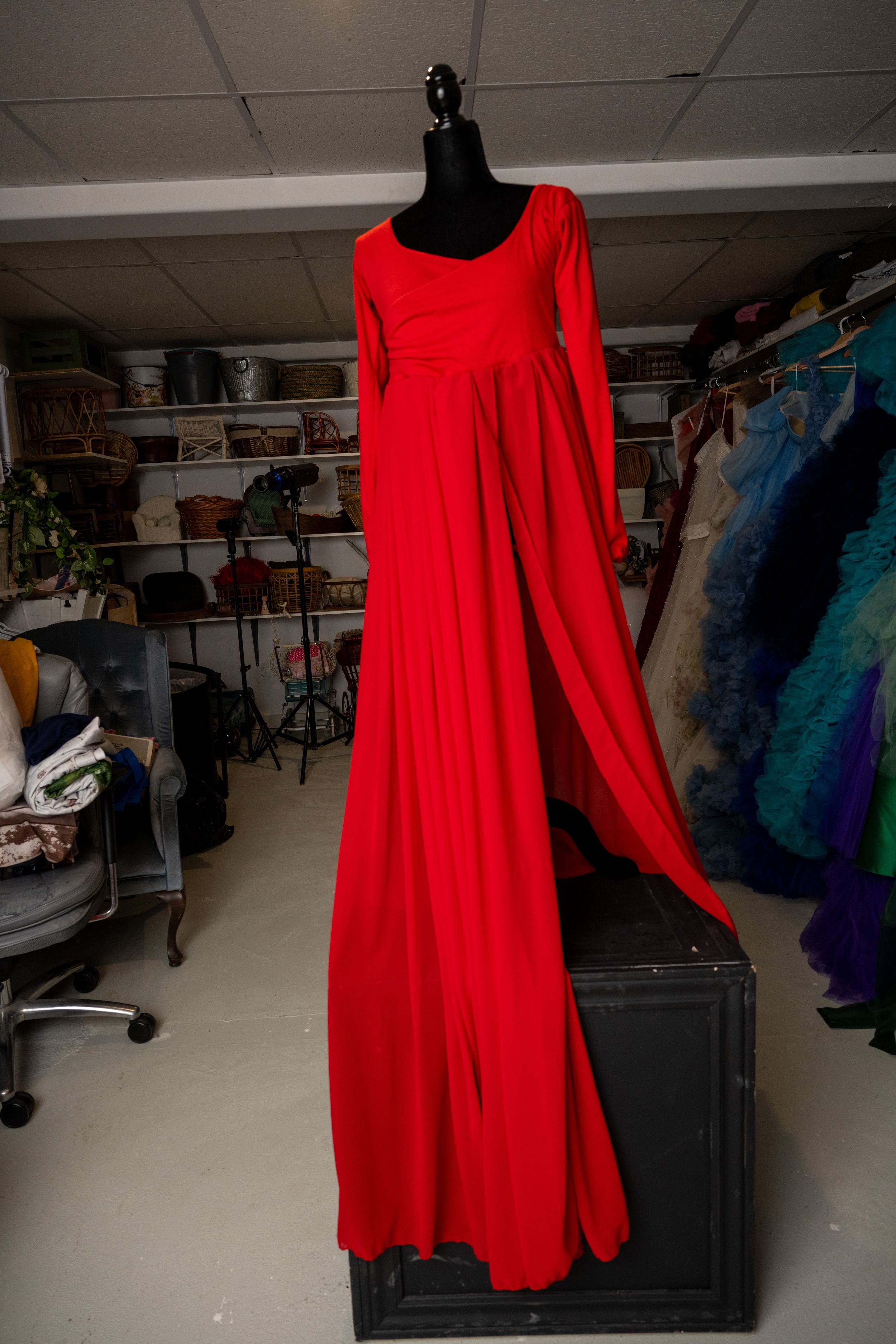 A bright red empire waist dress with long sleeves displayed on a black mannequin in a clothing store setting.
