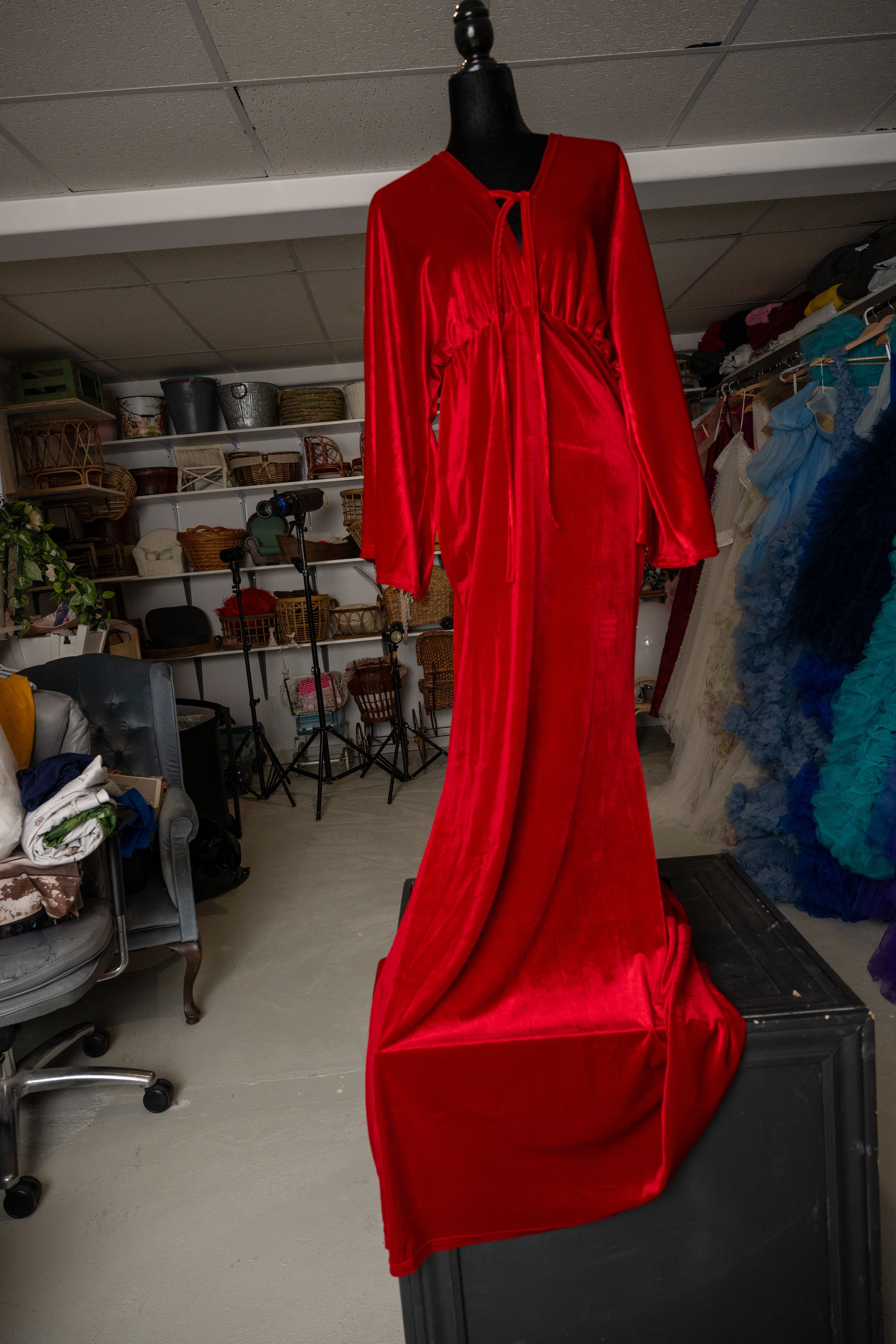 Red dress displayed on a mannequin in a cluttered storage room with clothing and shelving visible in background.