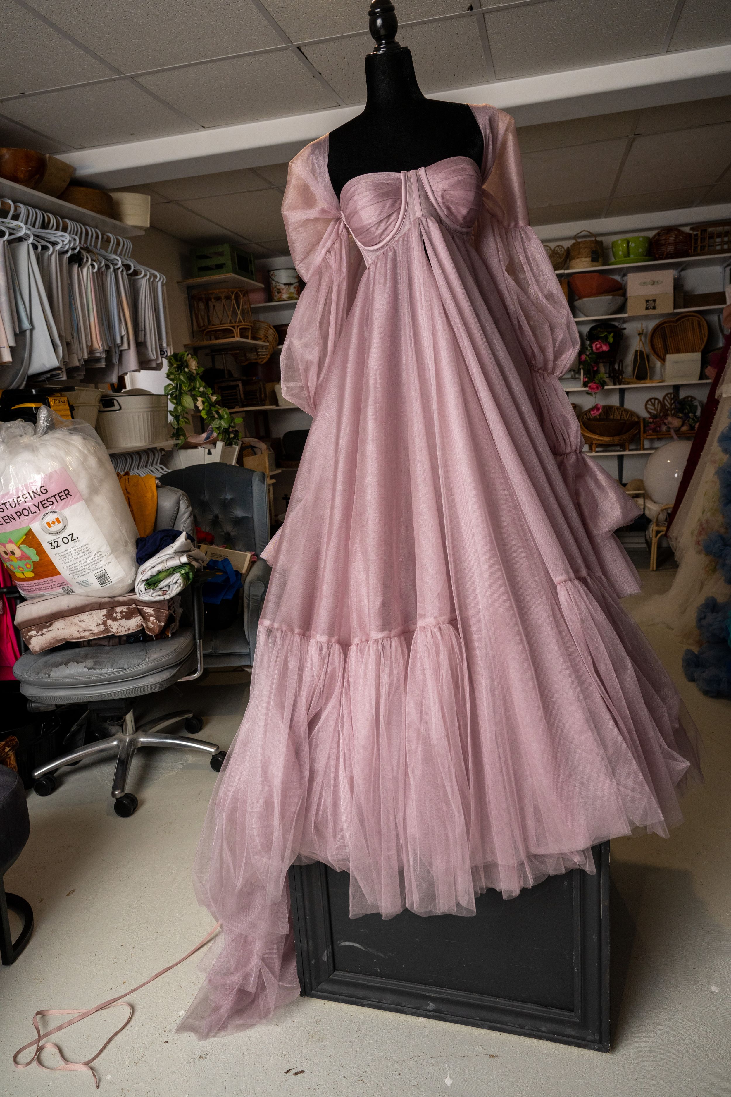 Dusty rose tulle gown with layered skirt shown on dress form in a creative workspace setting.