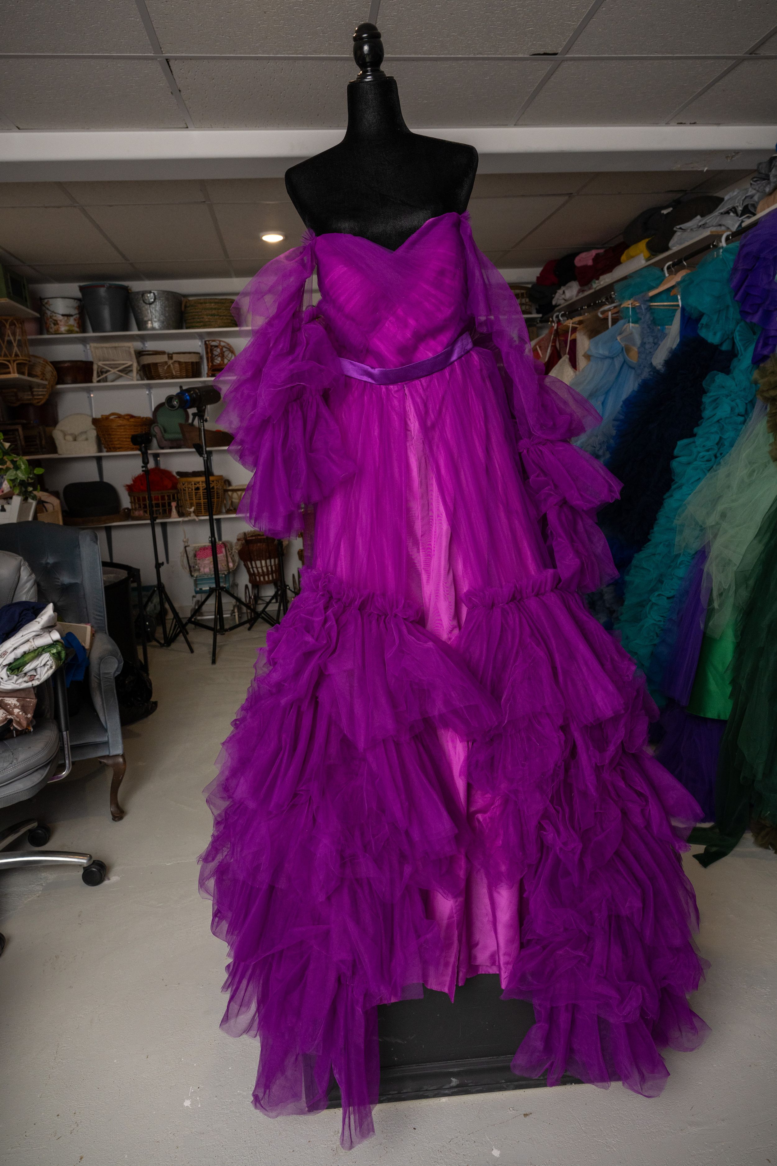 Vibrant magenta tulle evening gown with dramatic ruffled layers and off-shoulder design shown on dress form.