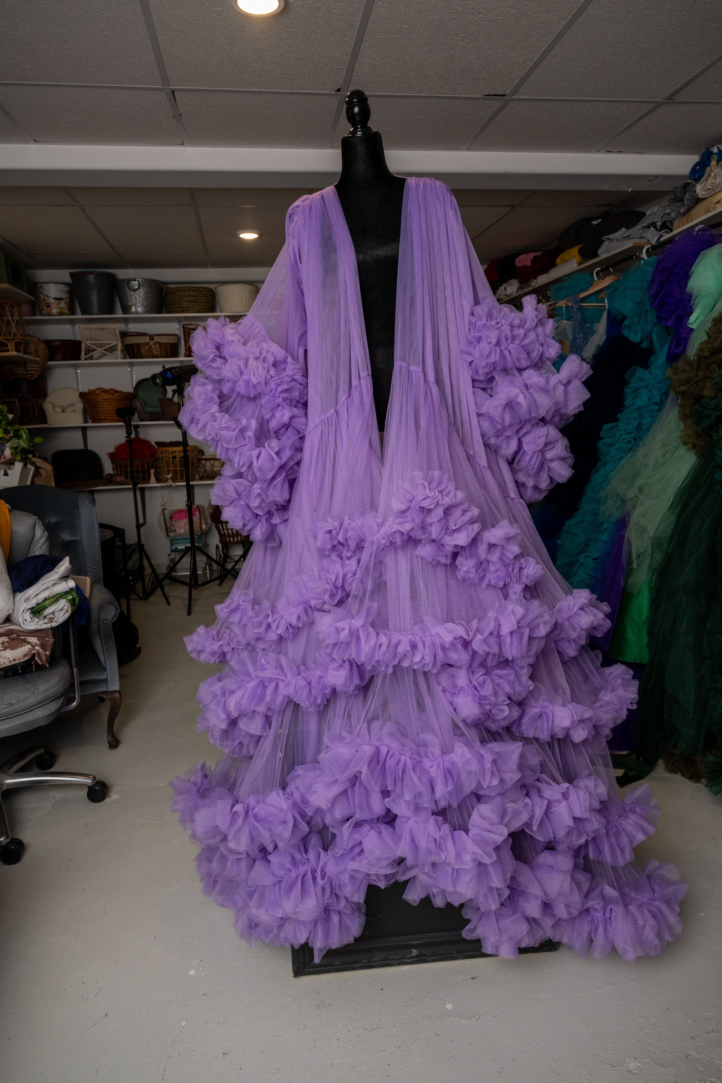 A dramatic lavender tulle robe with cascading ruffles hangs on a black mannequin in a costume storage room.