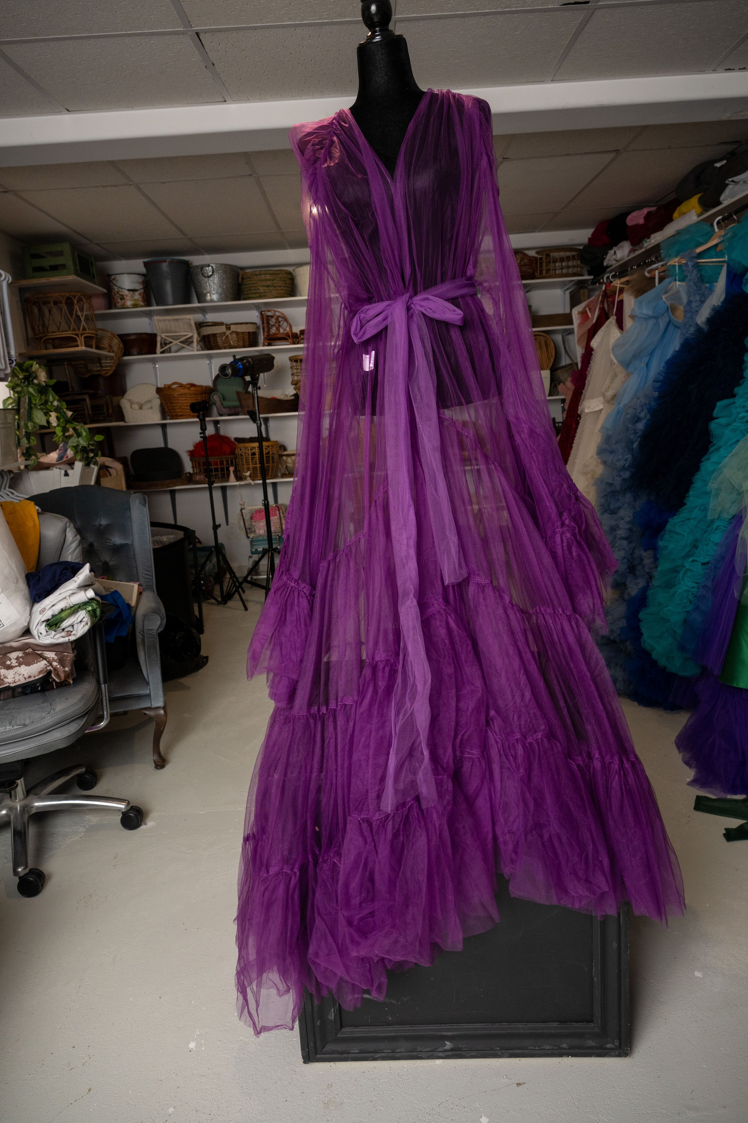 A vibrant purple tulle robe with dramatic flowing sleeves displayed on a black mannequin in a clothing studio.